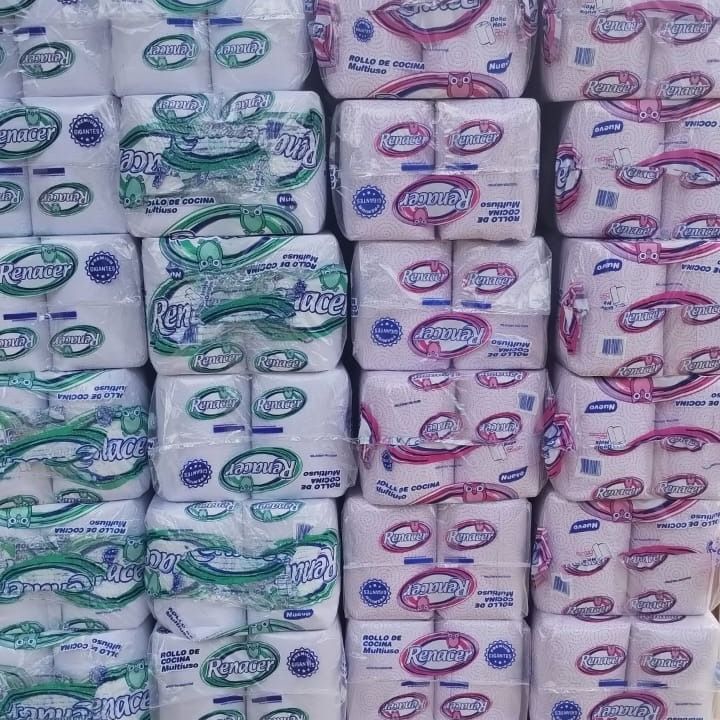 Pilas de toallas de papel empaquetadas, algunas verdes y blancas, otras rosas y blancas, apiladas en una tienda.