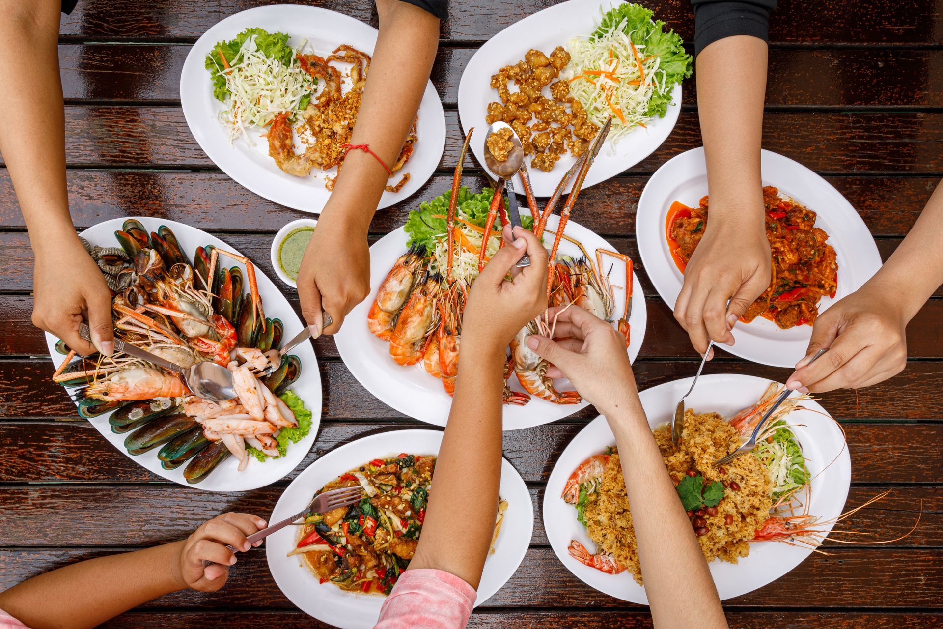Hands reaching over a table of assorted plated dishes during a shared meal Hands reaching over a table of assorted plated dishes during a shared meal