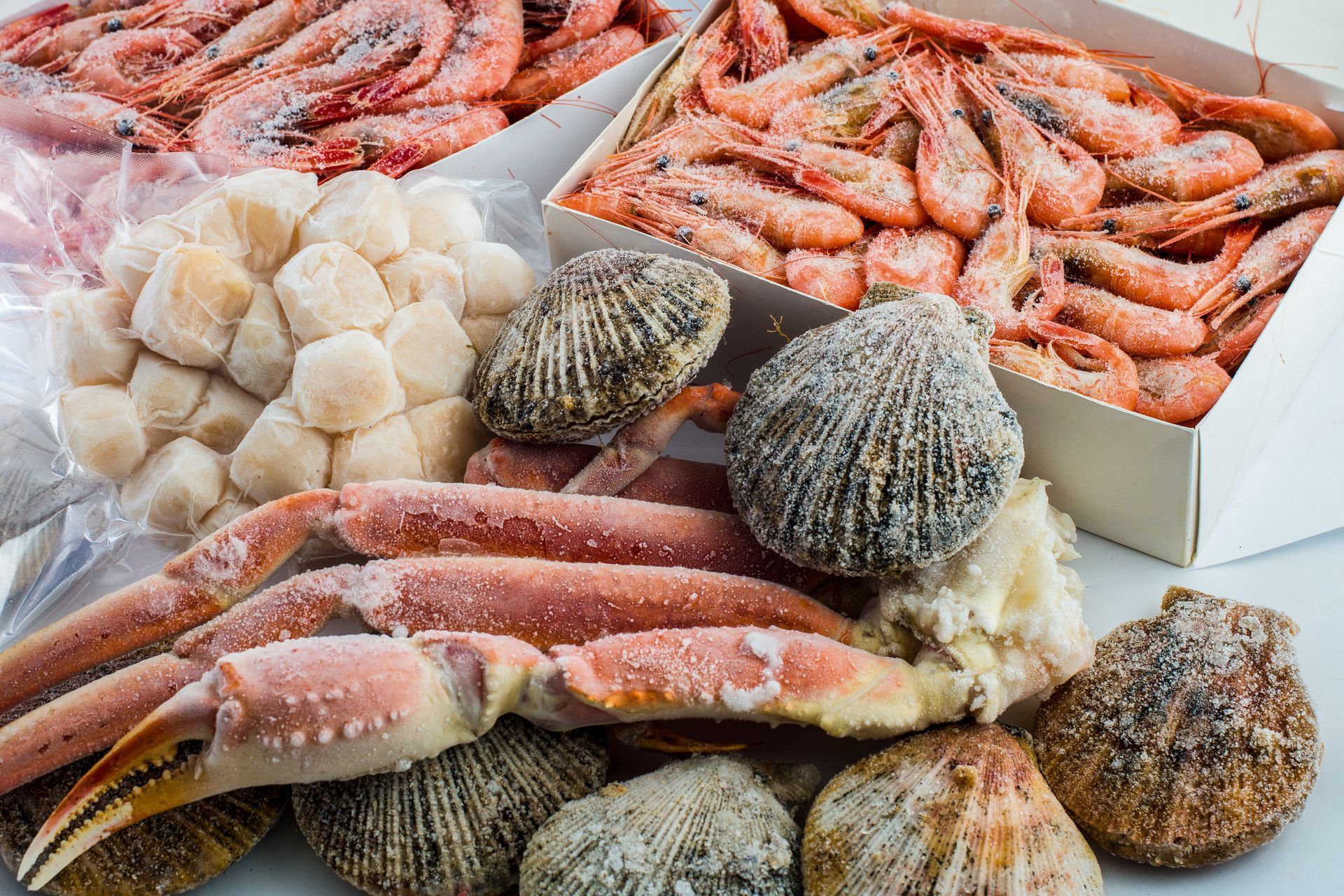 Frozen seafood assortment with shrimp, scallops, crab legs, and shellfish on ice in white trays Frozen seafood assortment with shrimp, scallops, crab legs, and shellfish on ice in white trays