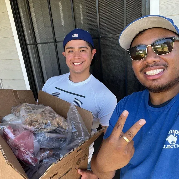 Two smiling people holding a box of clothes on a porch, one making a peace sign. Two smiling people holding a box of clothes on a porch, one making a peace sign.