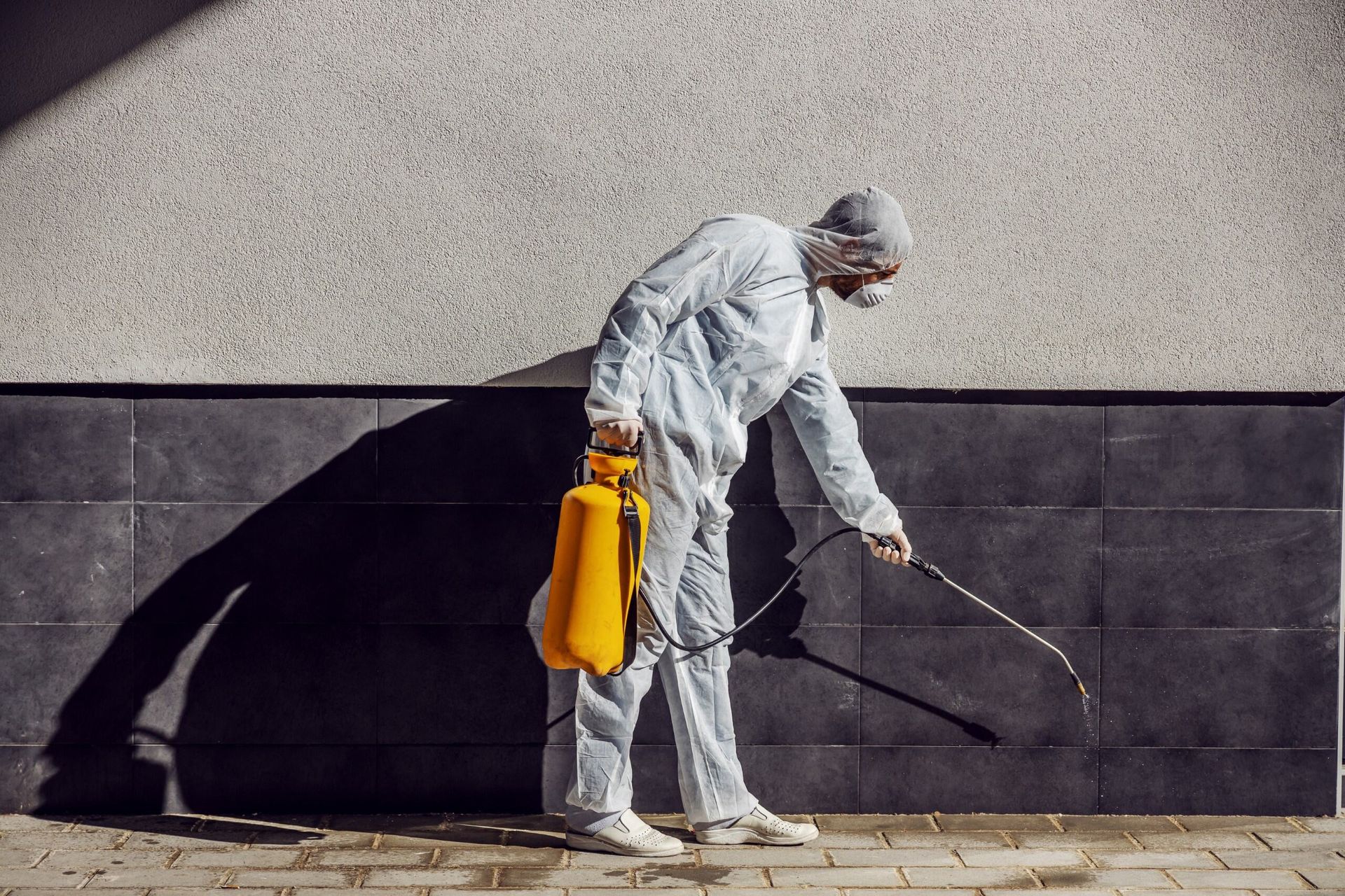 A Man in a Protective Suit is Spraying a Wall With a Sprayer — Lighthouse Pest Control In Alstonville, NSW
