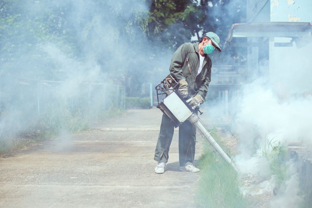 A Man Is Wearing a Mask and Using a Machine to Spray Smoke — Lighthouse Pest Control In Lennox Head, NSW