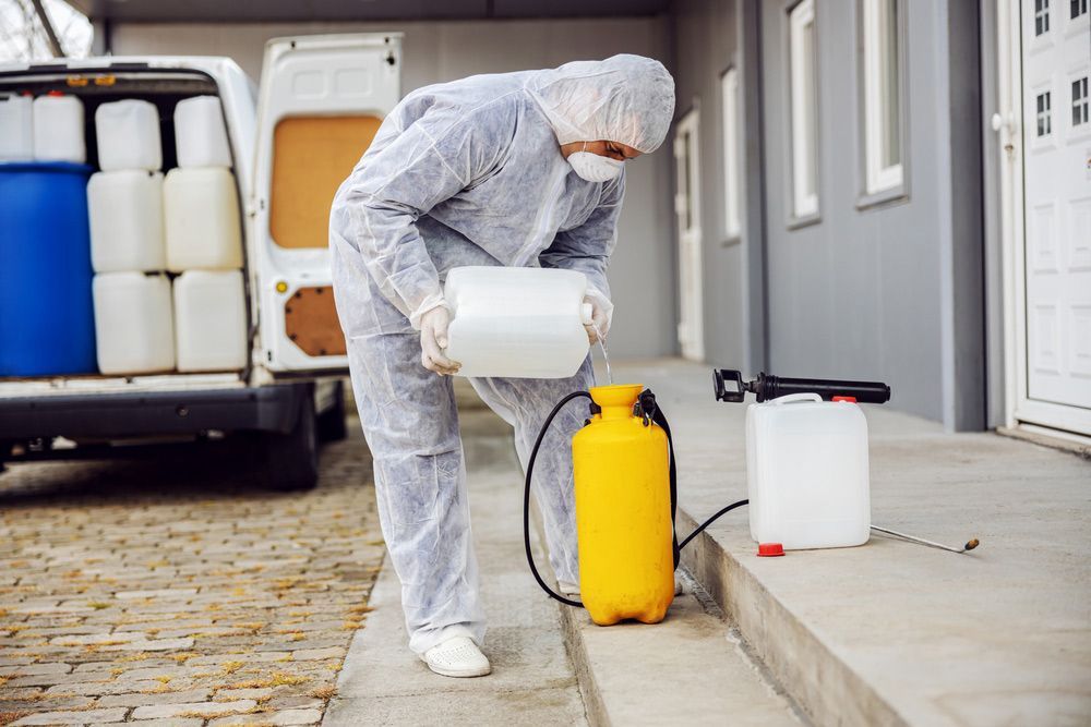 A Man in a Protective Suit is Spraying Chemicals on the Ground — Lighthouse Pest Control In Byron Bay, NSW