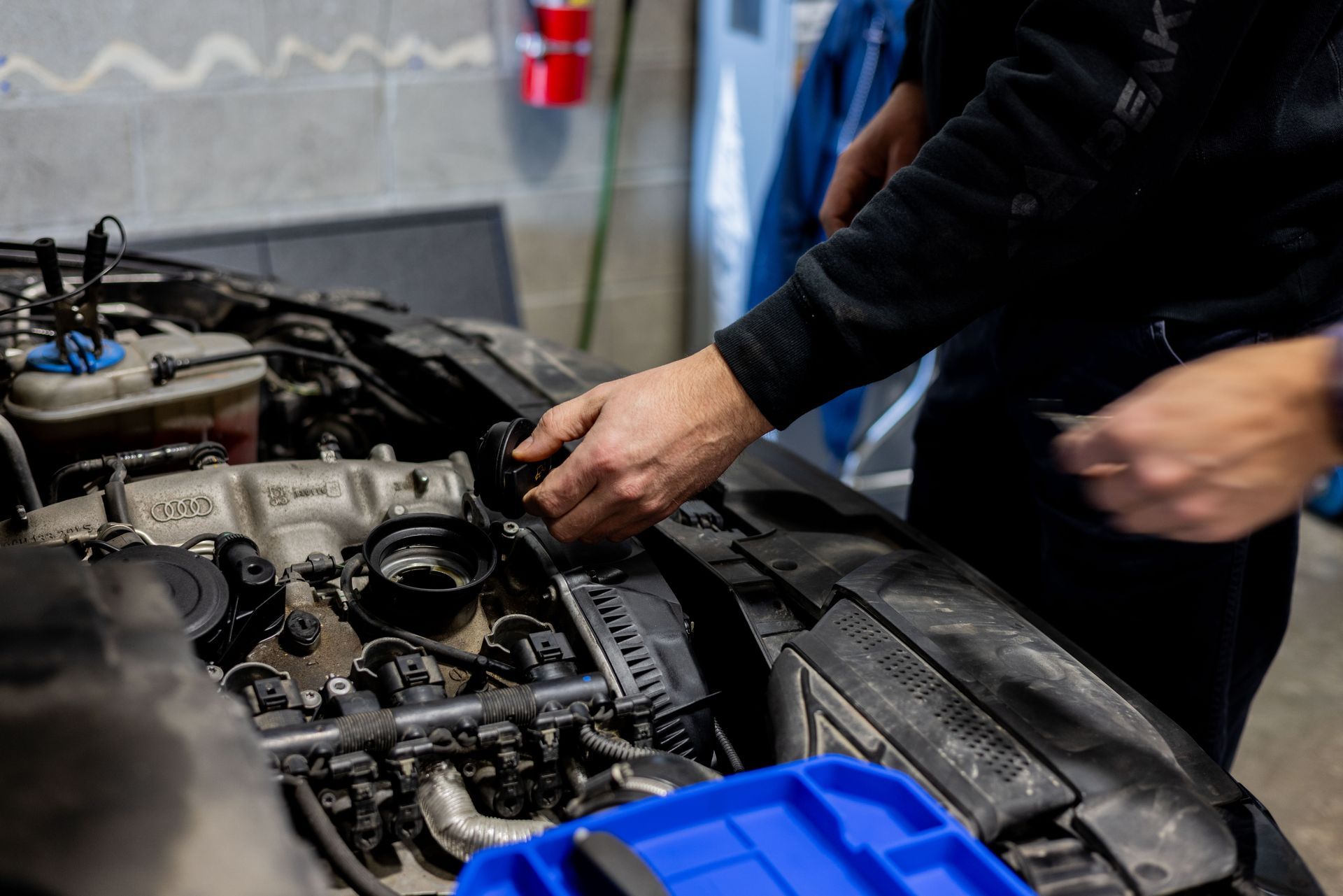 Person working on a car engine, hands on the open compartment in a garage.