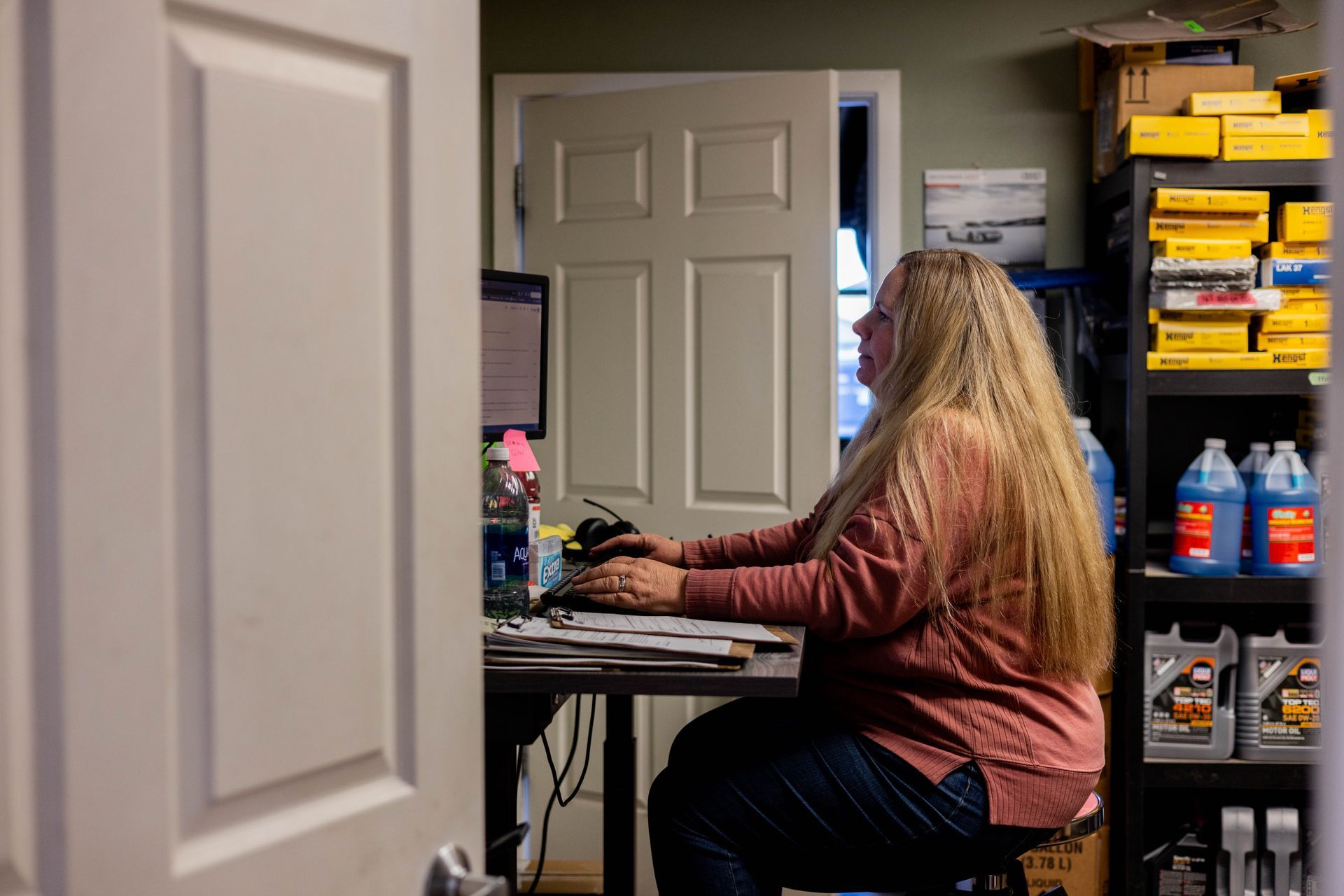 Woman with long blonde hair works at a computer in a cluttered office; door and shelves in the background.| Peak Euro