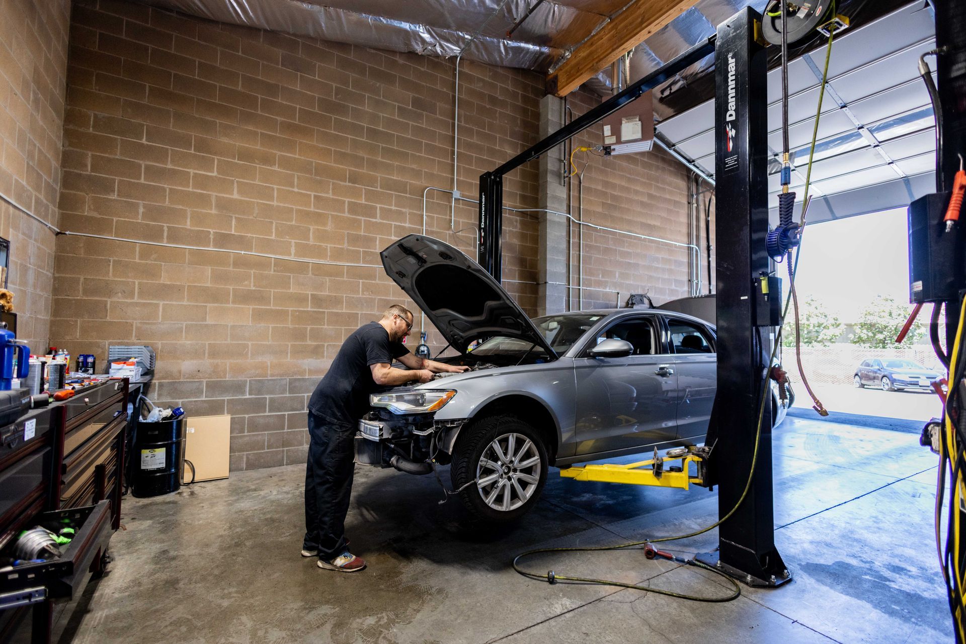 Mechanic working on a silver car raised on a lift inside a garage. | Peak Euro