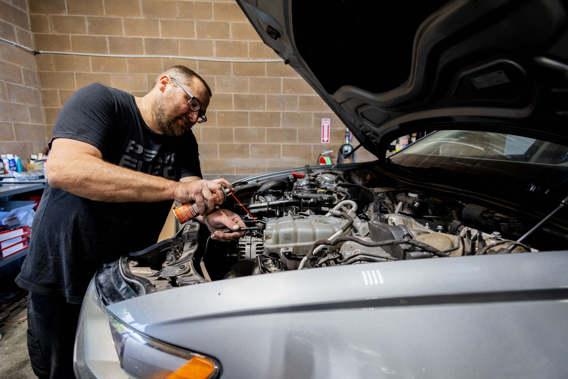 Mechanic working on a car engine with open hood in a garage. | Peak Euro