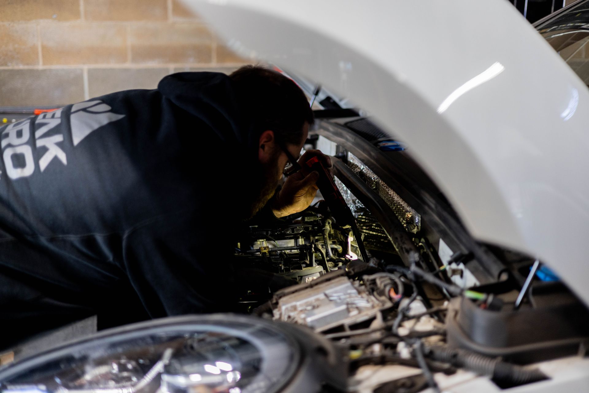 Man in black hoodie working on a car engine, white exterior.| Peak Euro