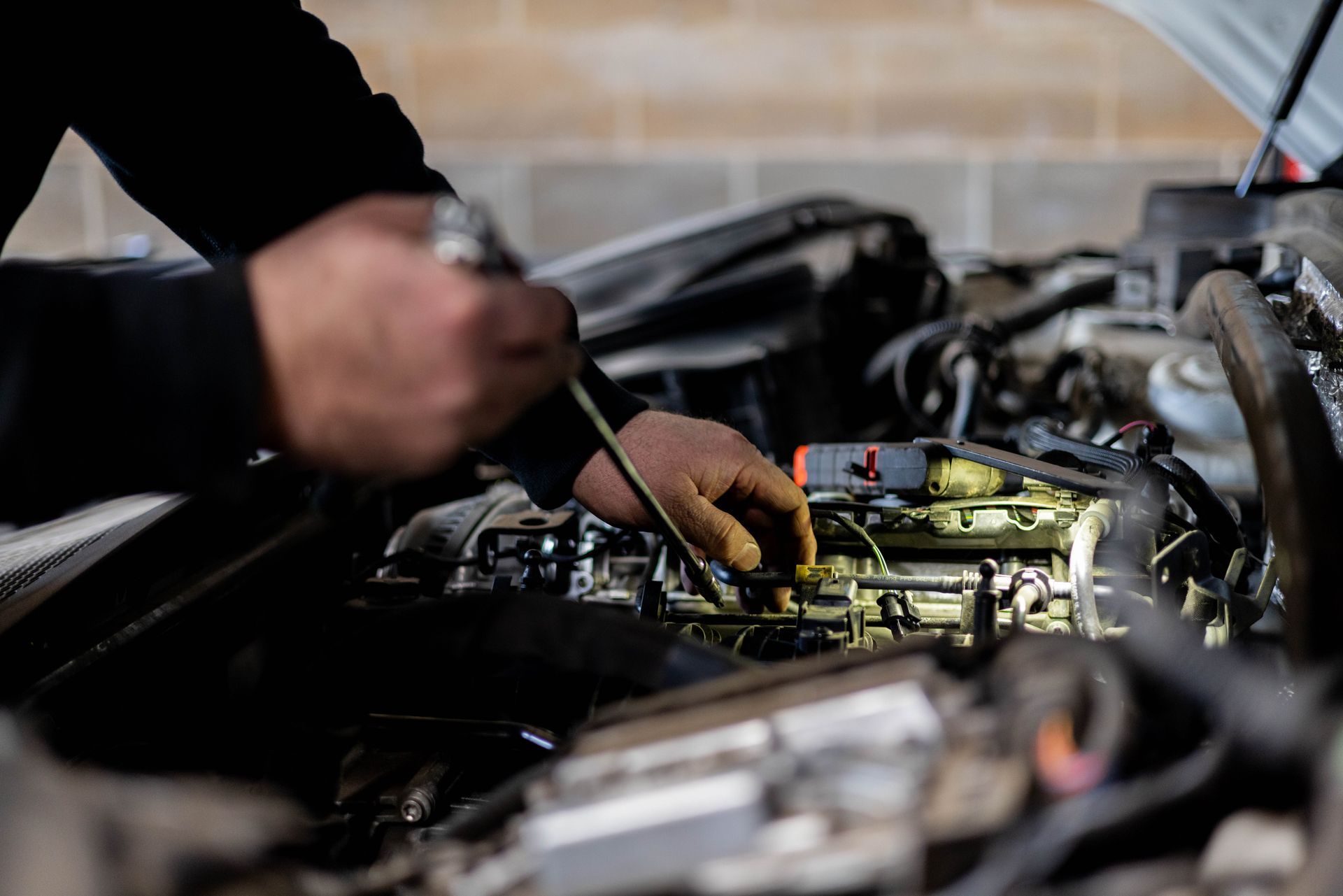 Mechanic working on a car engine, holding a tool with a flashlight in a garage.| Peak Euro