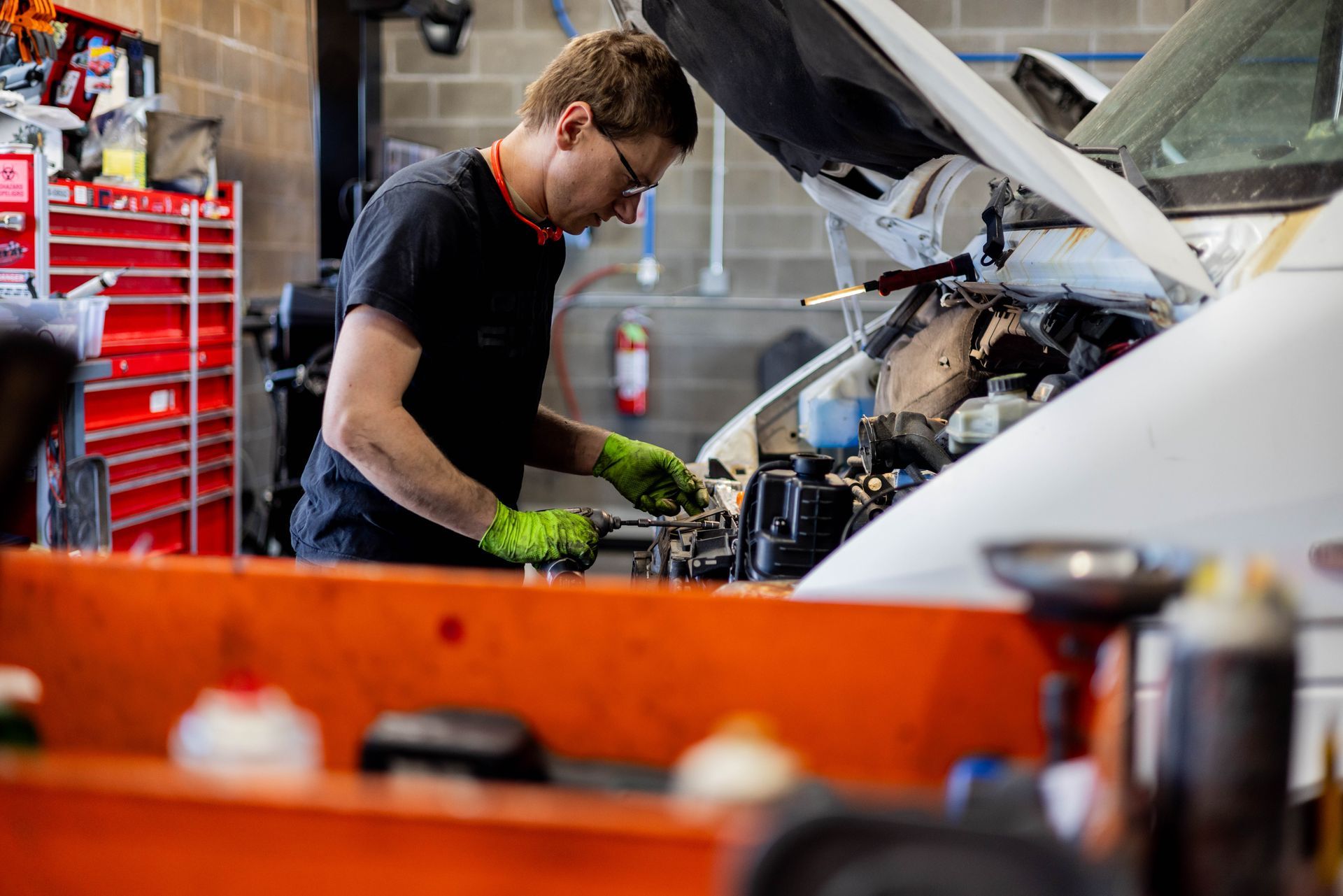 Mechanic in a garage working on a vehicle engine, wearing gloves. | Peak Euro