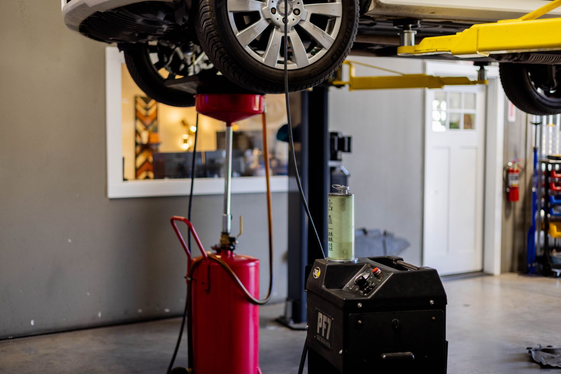 Car on a lift being serviced; oil draining into a red container in a garage. | Peak Euro