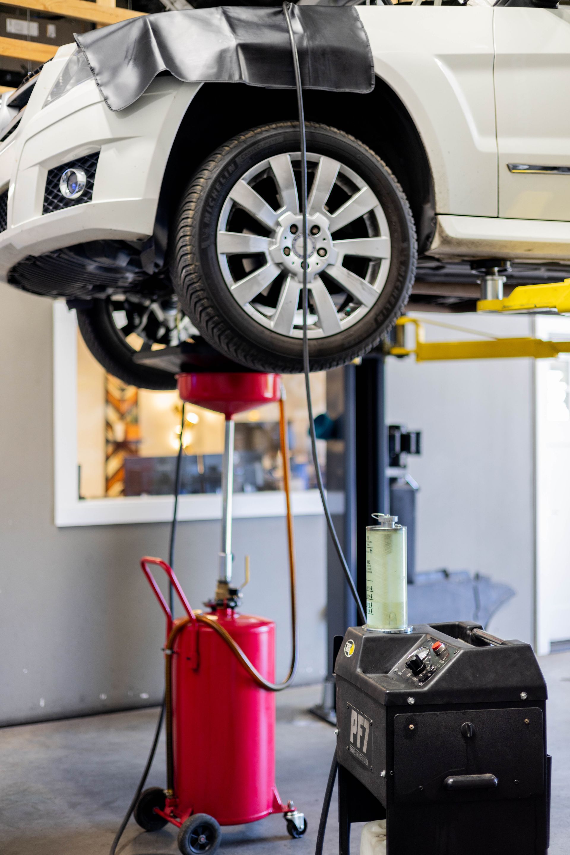 White car on a lift being serviced; oil draining into a red container at an auto repair shop. | Peak Euro