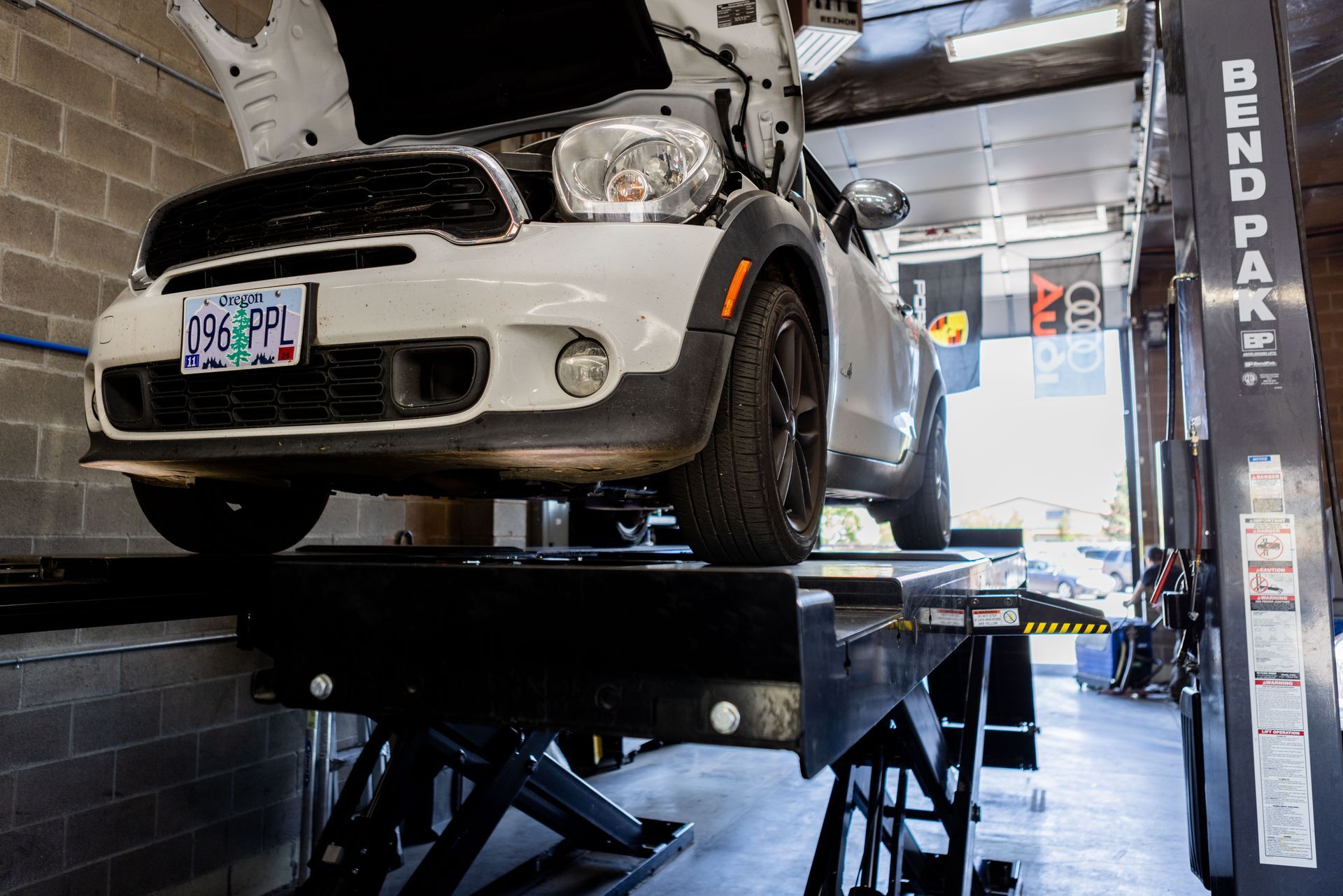White Mini Cooper on a car lift in a garage with the hood open for maintenance. | Peak Euro