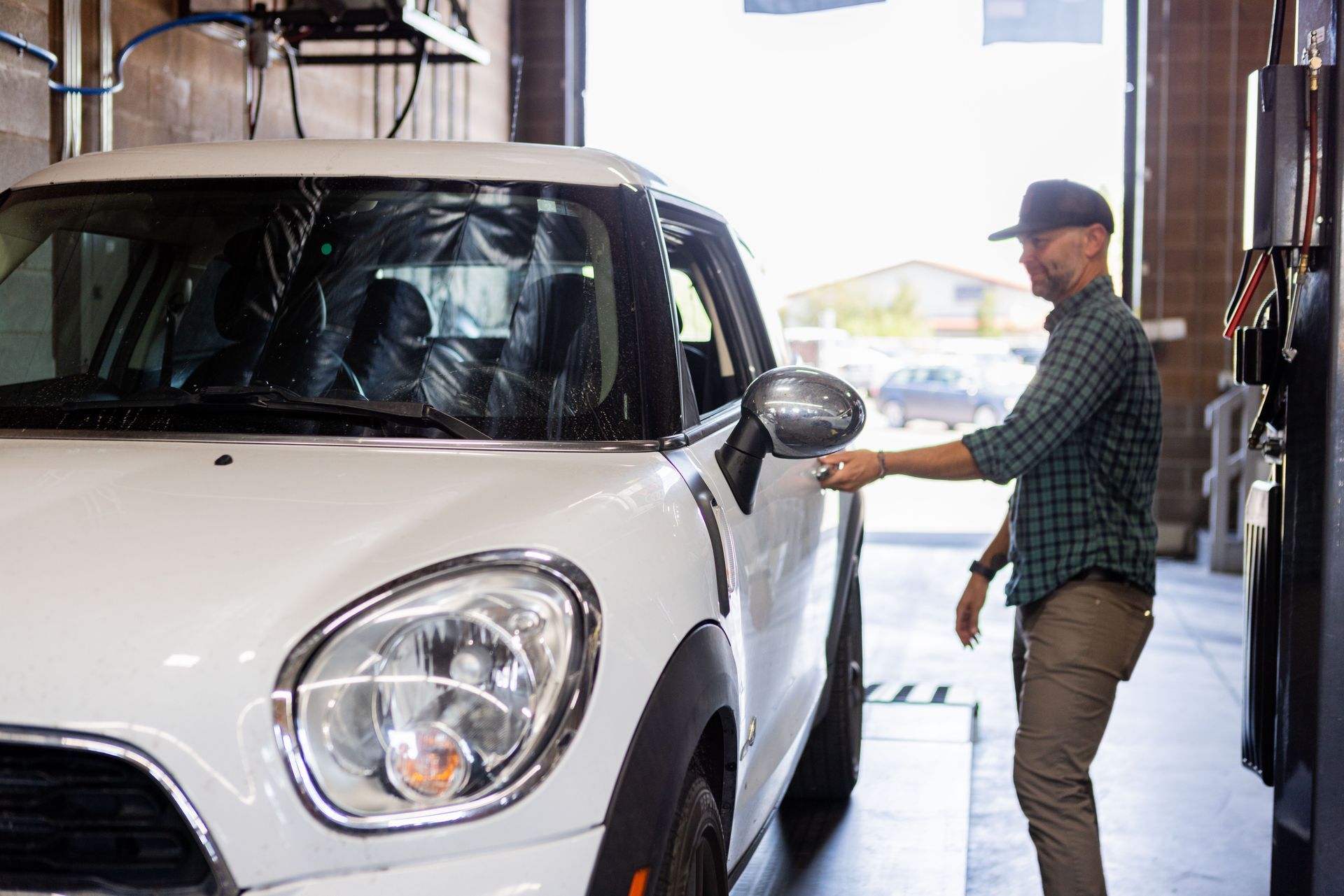 Man inspecting a white Mini Cooper in a garage, adjusting the side mirror. | Peak Euro