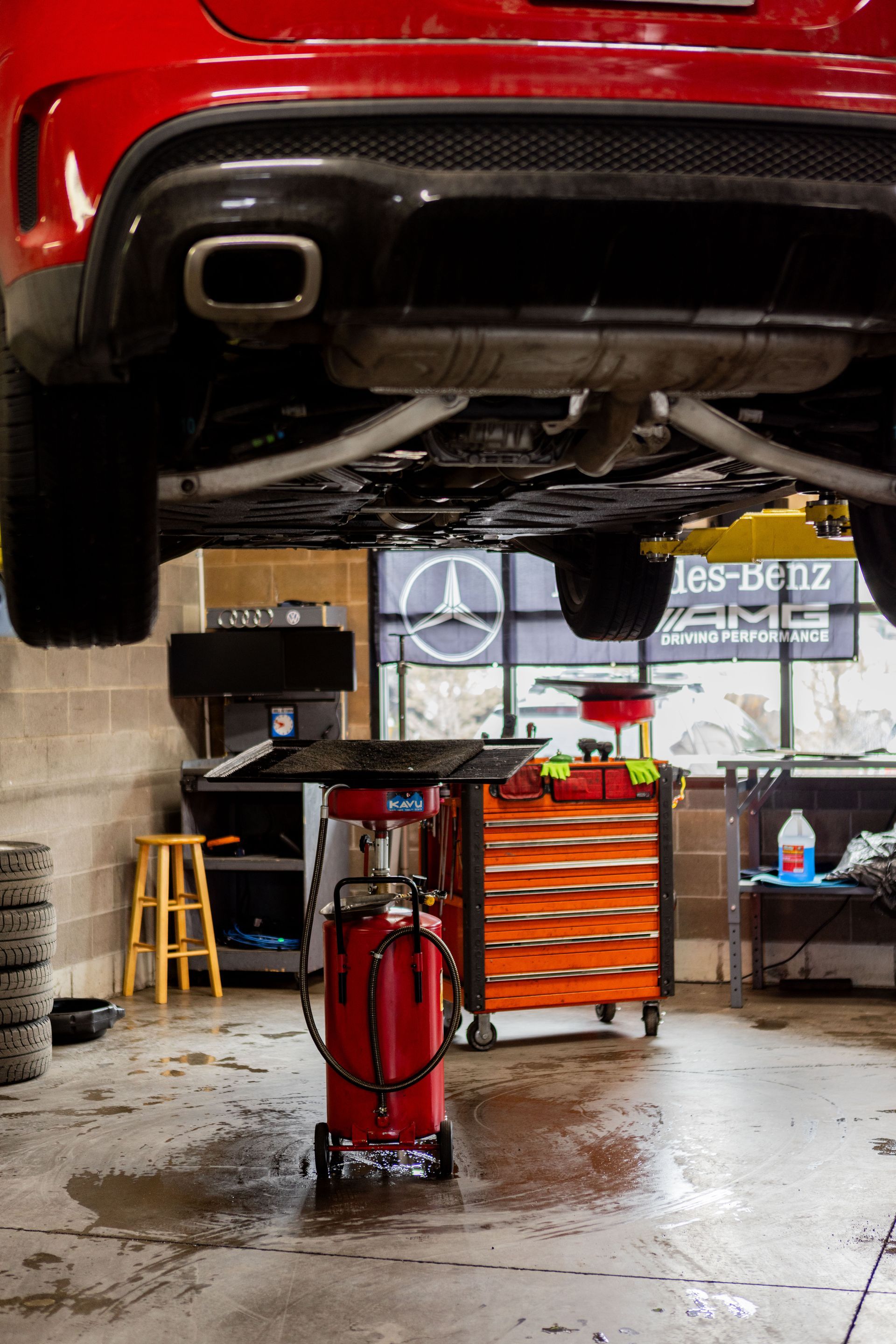 Red car raised in auto shop; tools and a Mercedes-Benz logo are visible.| Peak Euro
