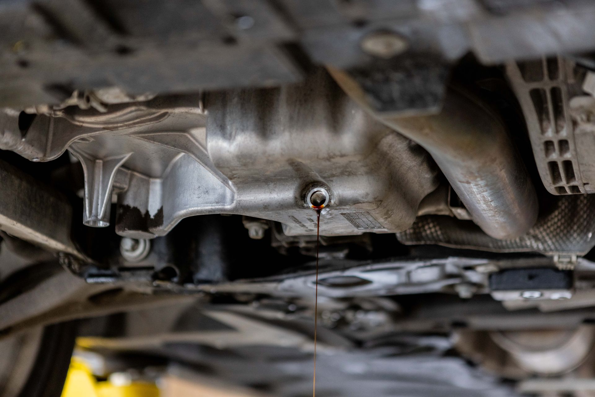 Underneath a vehicle, oil drains from a drain plug.| Peak Euro