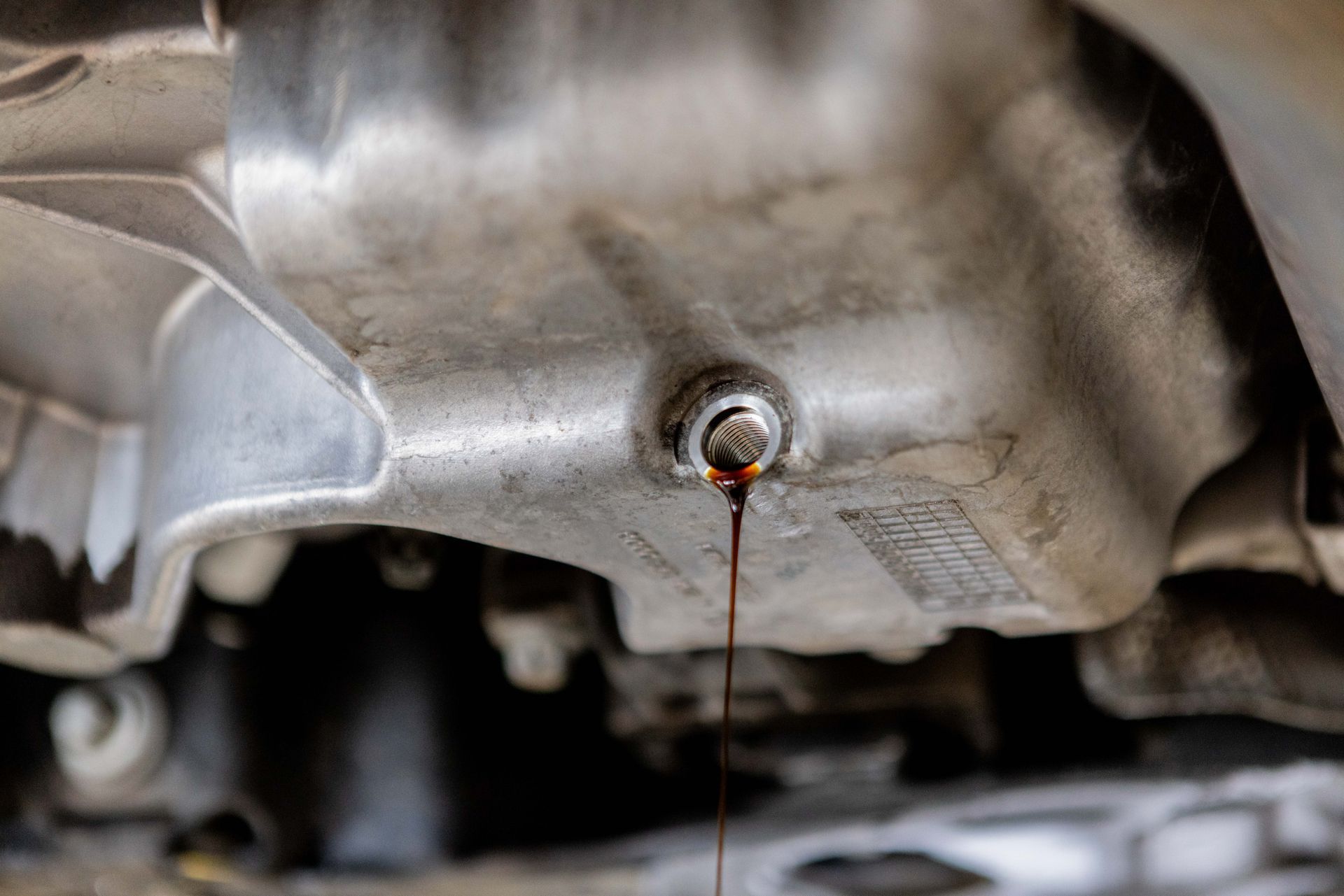 Oil draining from a car's oil pan, revealing the underside of the engine.