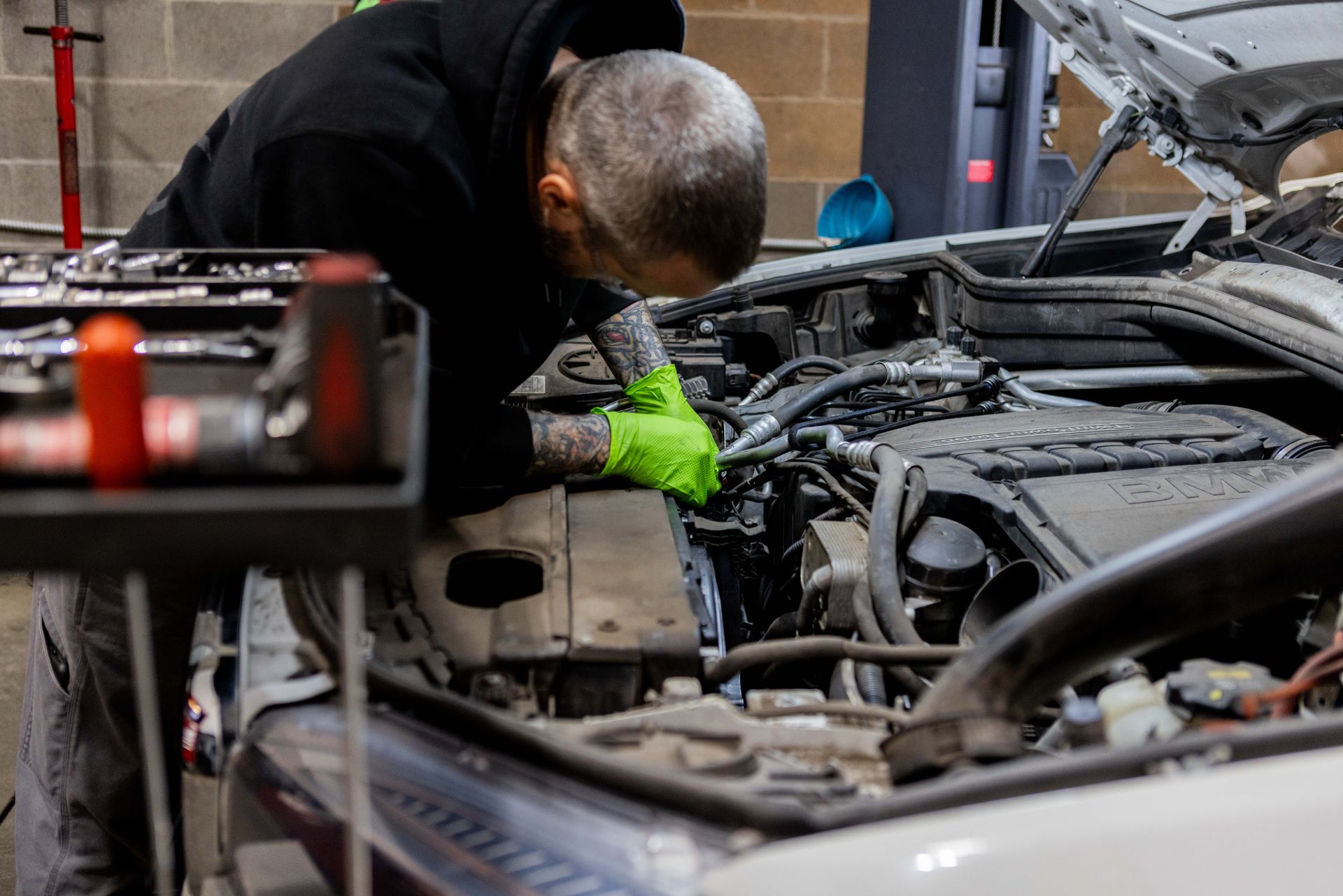 Mechanic working on a car engine. Wearing green gloves, in a garage setting.