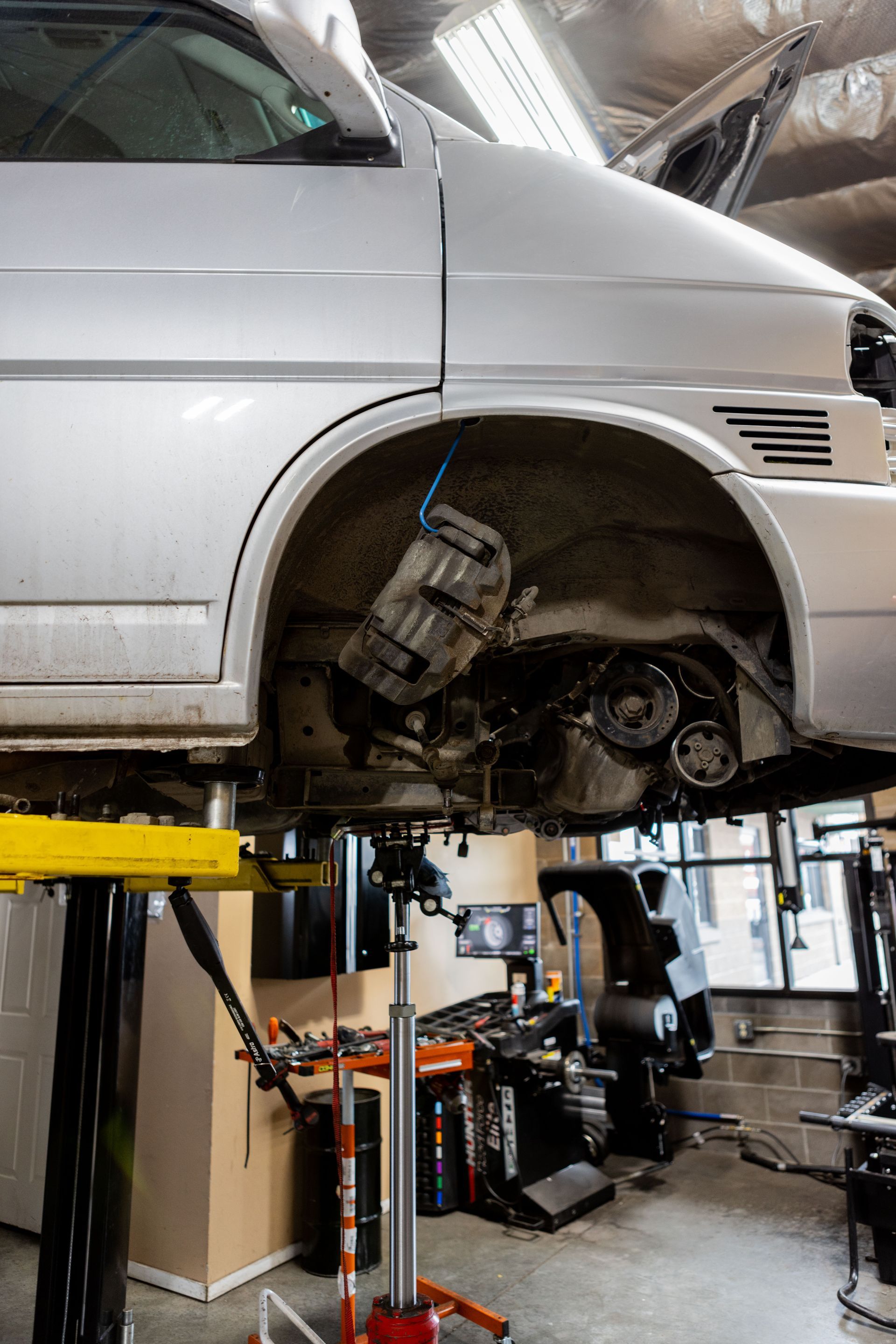 A silver van hoisted on a lift in a garage, its engine exposed for repair.