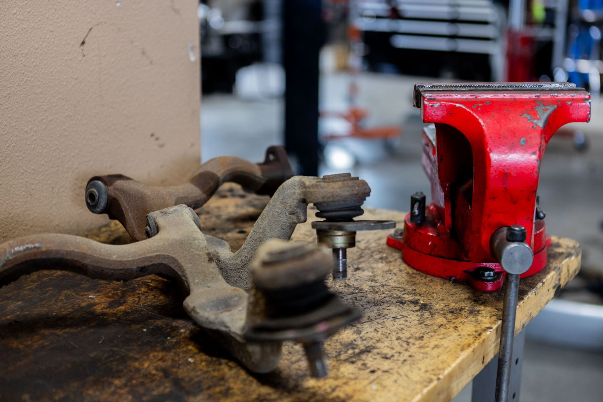 Rust-covered car suspension parts on a workbench next to a red vise in a garage setting.