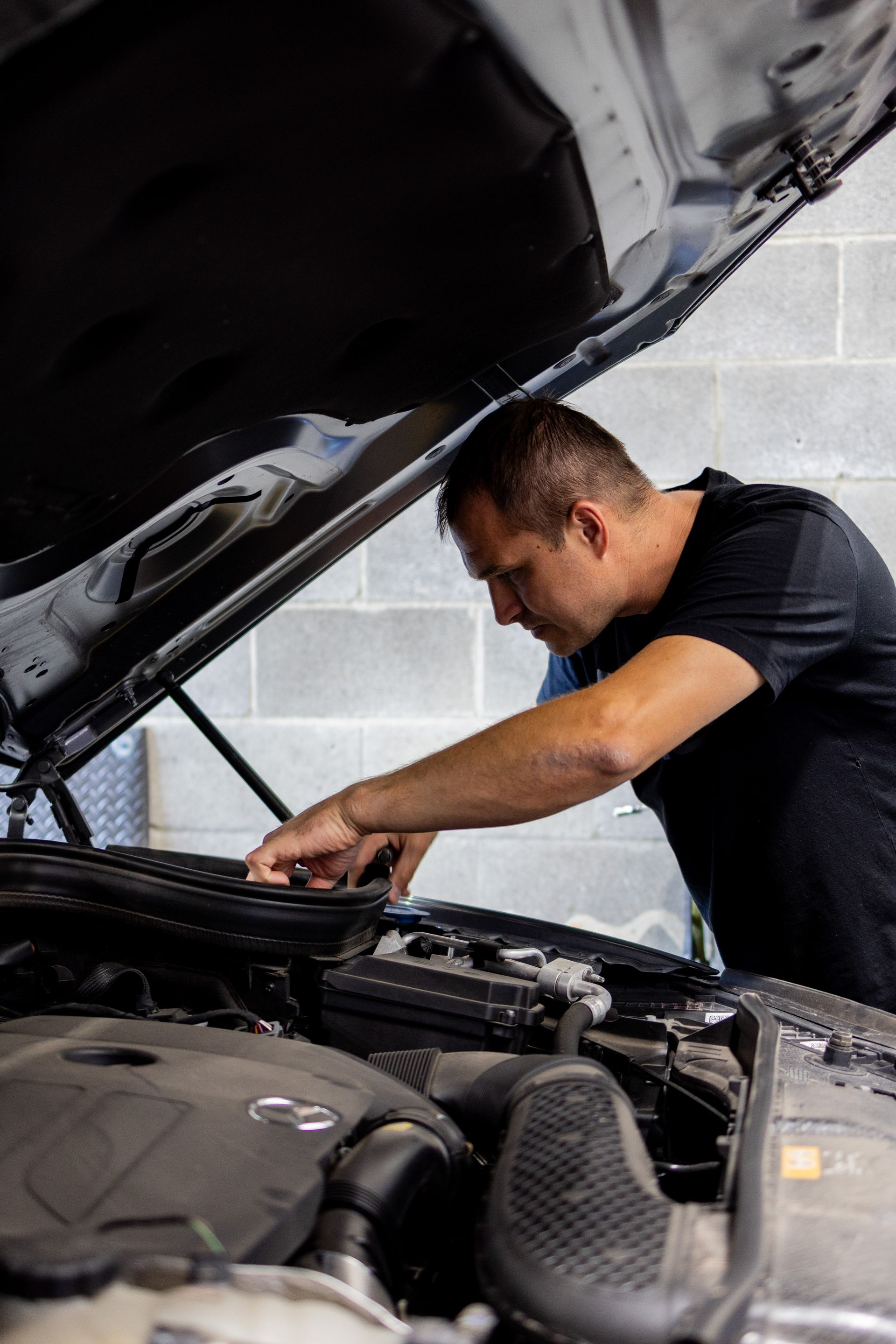 Mechanic works under the hood of a car, inspecting engine parts. | Peak Euro