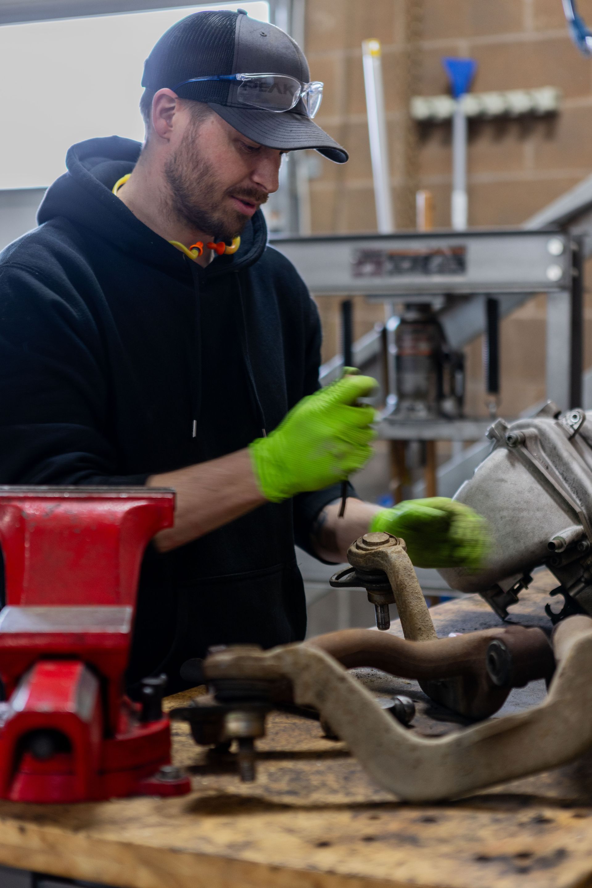 Man in workshop, using tool on engine parts, wearing gloves and safety glasses.