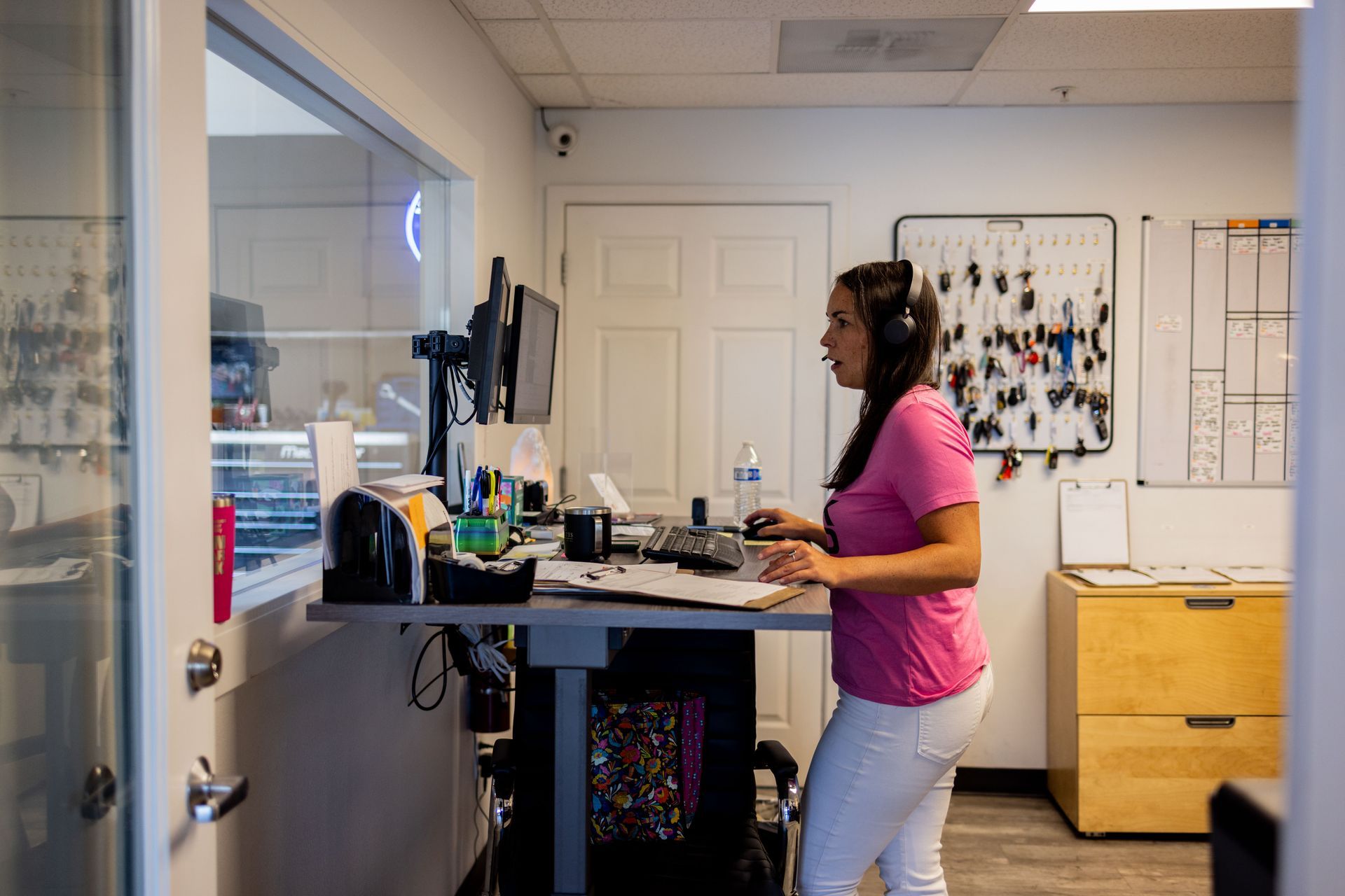 Woman wearing headset stands at a desk in an office. She types on a keyboard. | Peak Euro