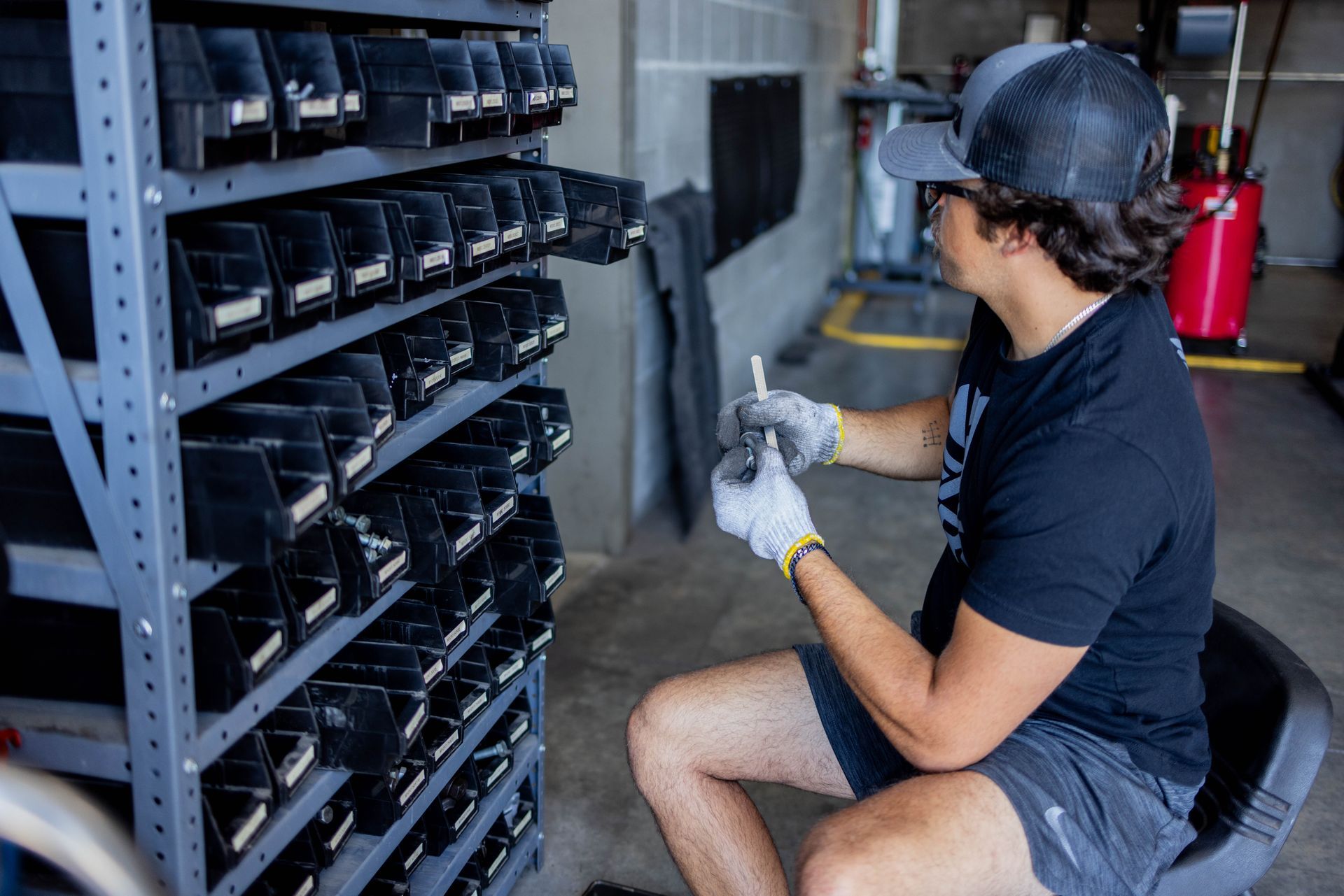 Man in black shirt sorting parts from shelves in a shop, wearing gloves. | Peak Euro