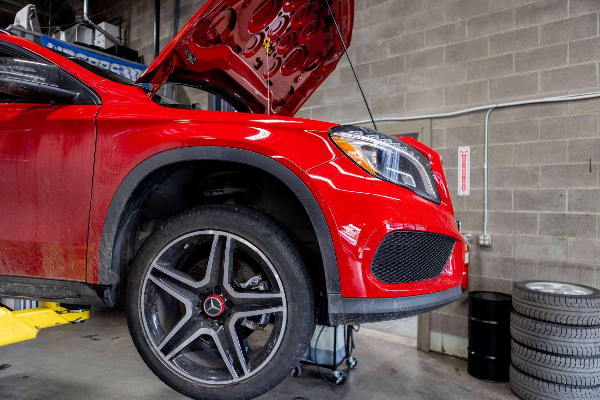 Red Mercedes SUV with hood open in a garage, tires stacked nearby. | Peak Euro