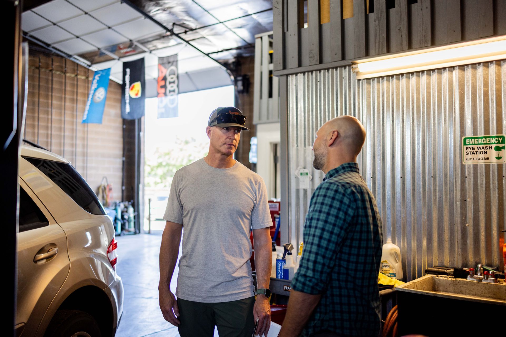 Two men talking in a garage. One in a gray shirt, the other in a blue plaid shirt, with a car in the background. | Peak Euro