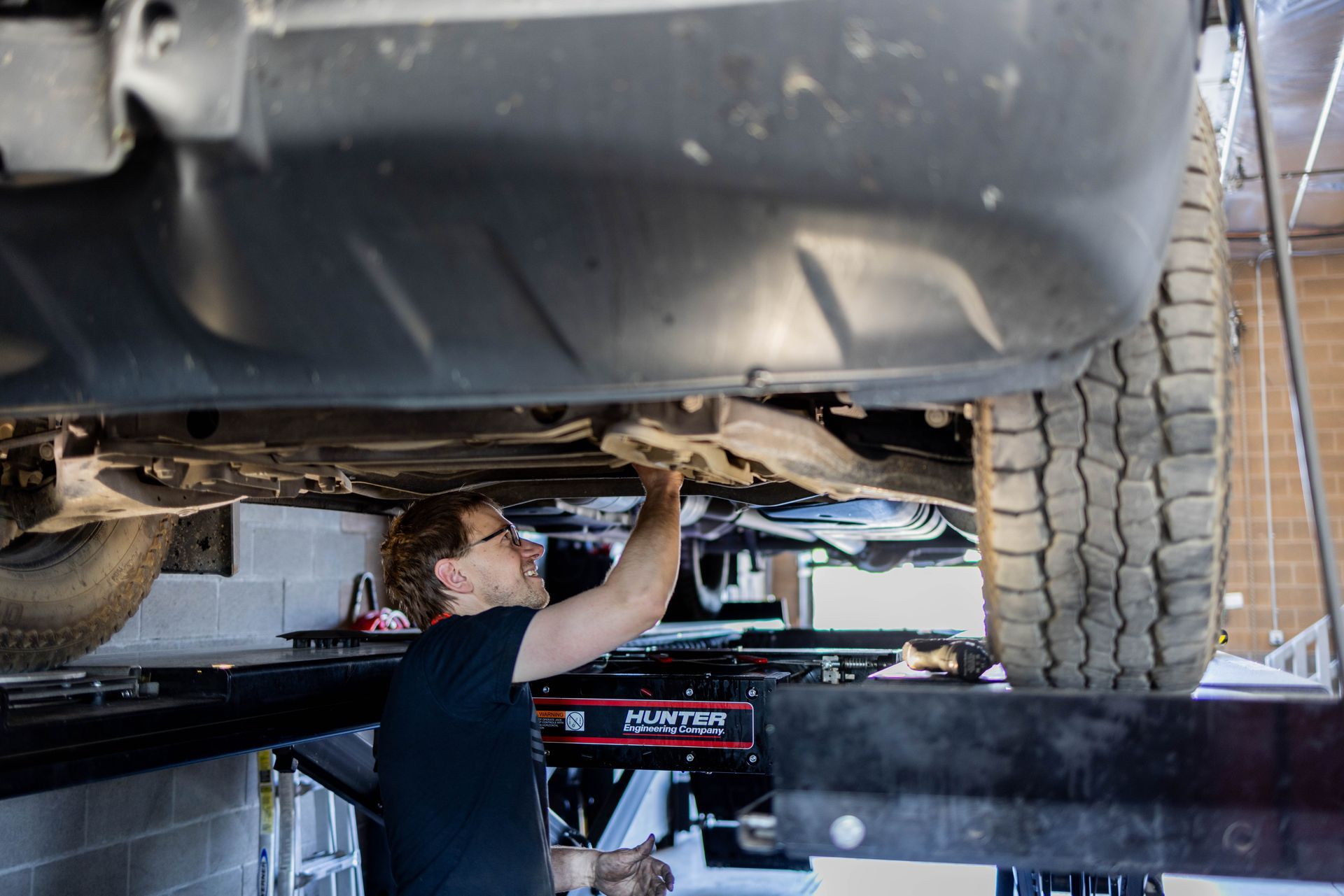Mechanic working under a car lifted on a hoist in a garage. | Peak Euro