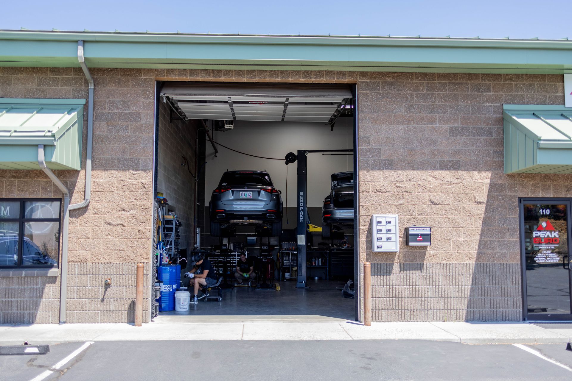 Car in a garage bay on a lift. Brick building, open door, equipment visible. | Peak Euro