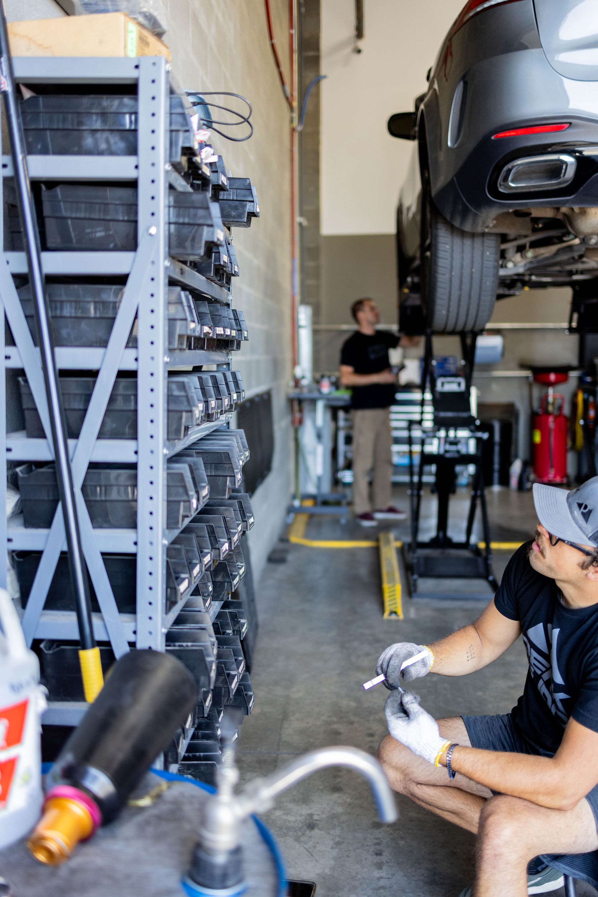 Mechanics working on a car in a garage. One kneels with tools, another examines the vehicle. | Peak Euro