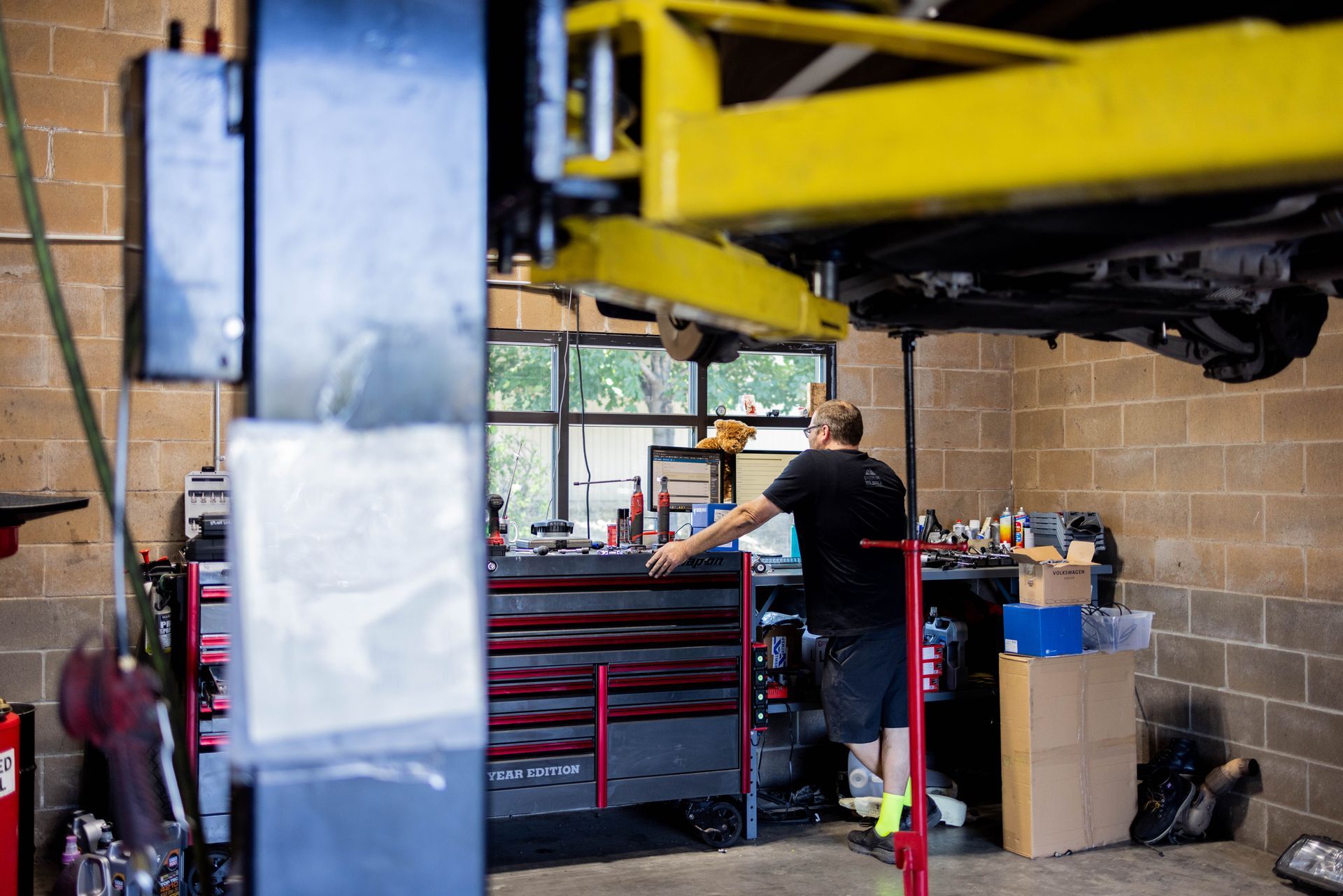 Mechanic working on a car raised on a yellow lift in a garage, reaching for tools. | Peak Euro