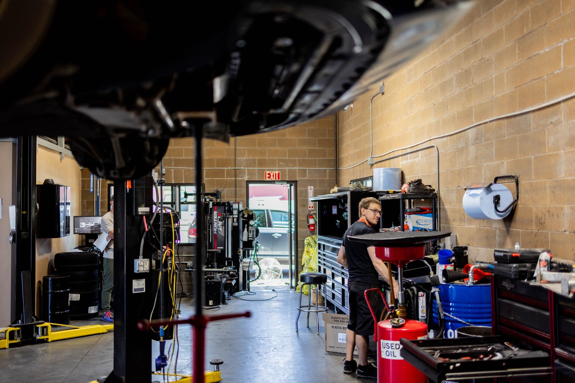 Mechanic working under a car raised on a lift in an auto shop. Interior shot with tools and equipment. | Peak Euro