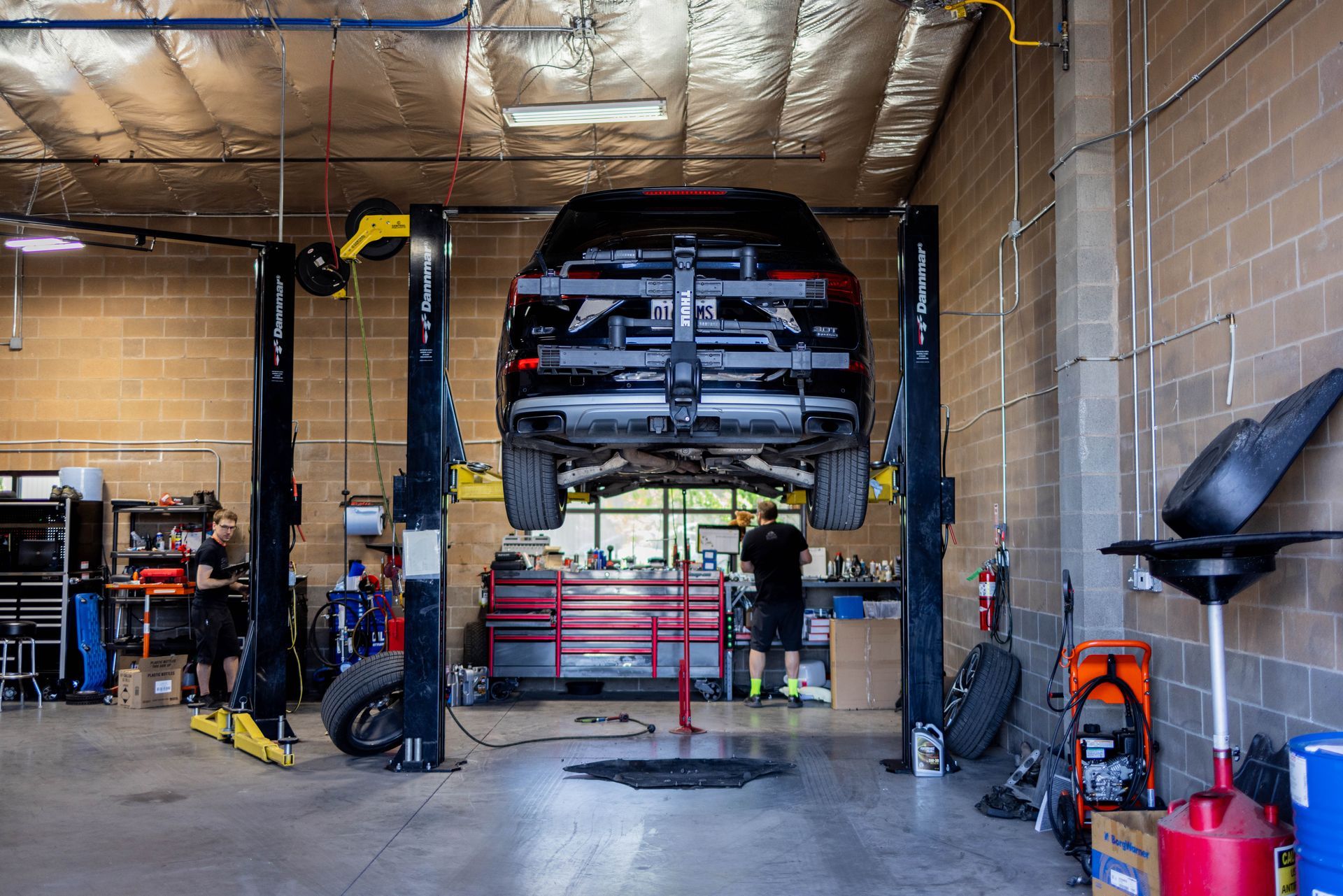 Black SUV on a hydraulic lift in a car repair shop; two mechanics working. | Peak Euro