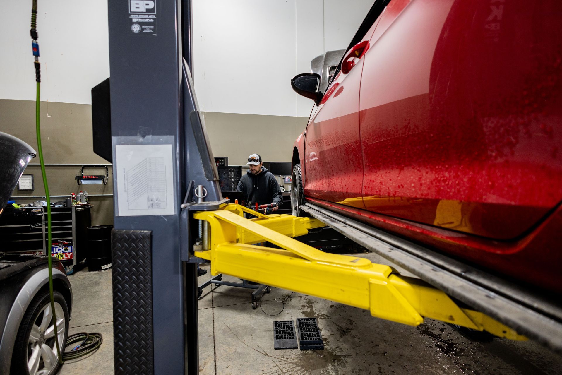 A mechanic working under a red car lifted on a yellow auto lift inside a garage.| Peak Euro