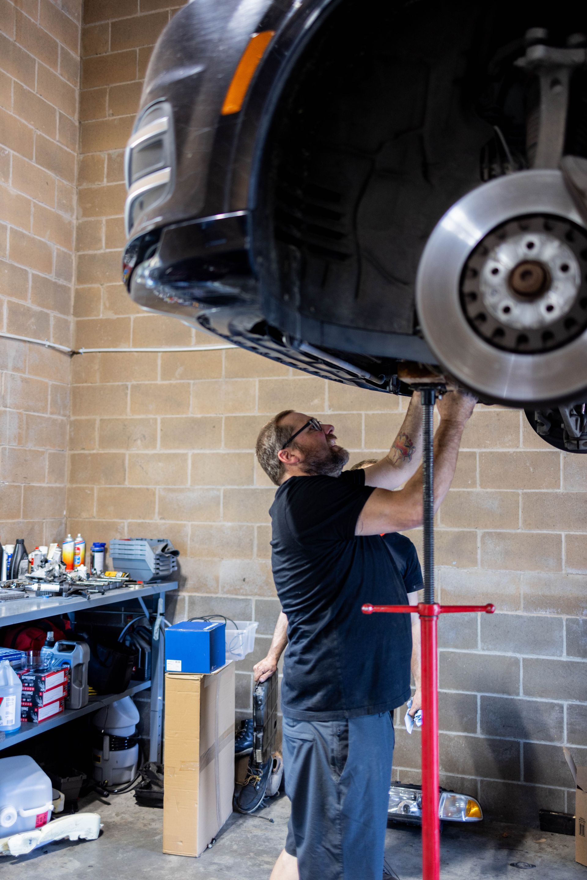 Mechanic working on car suspended on lift in a brick-walled garage. | Peak Euro