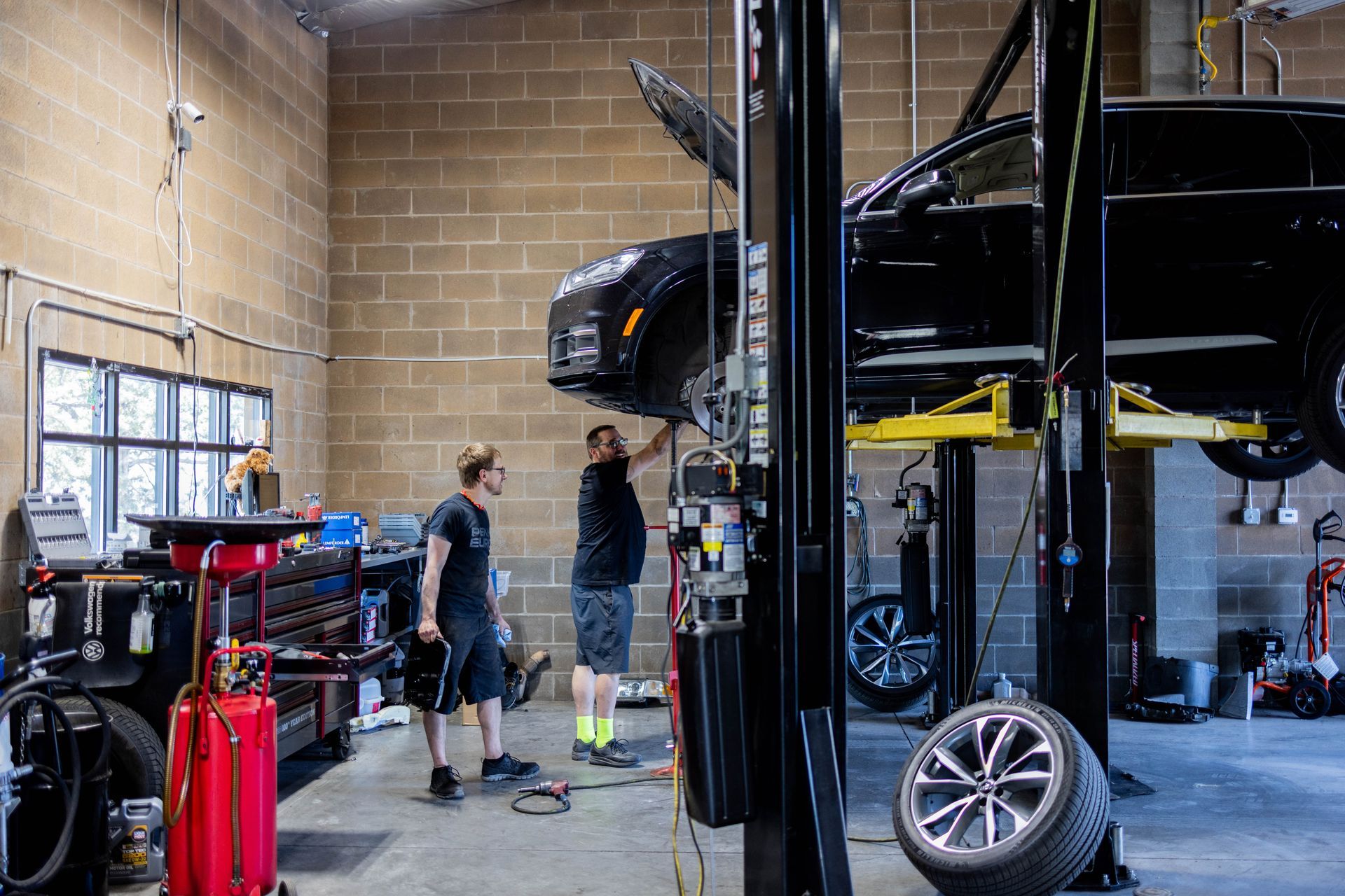 Two mechanics working on a black SUV lifted in a garage. One tire removed. | Peak Euro