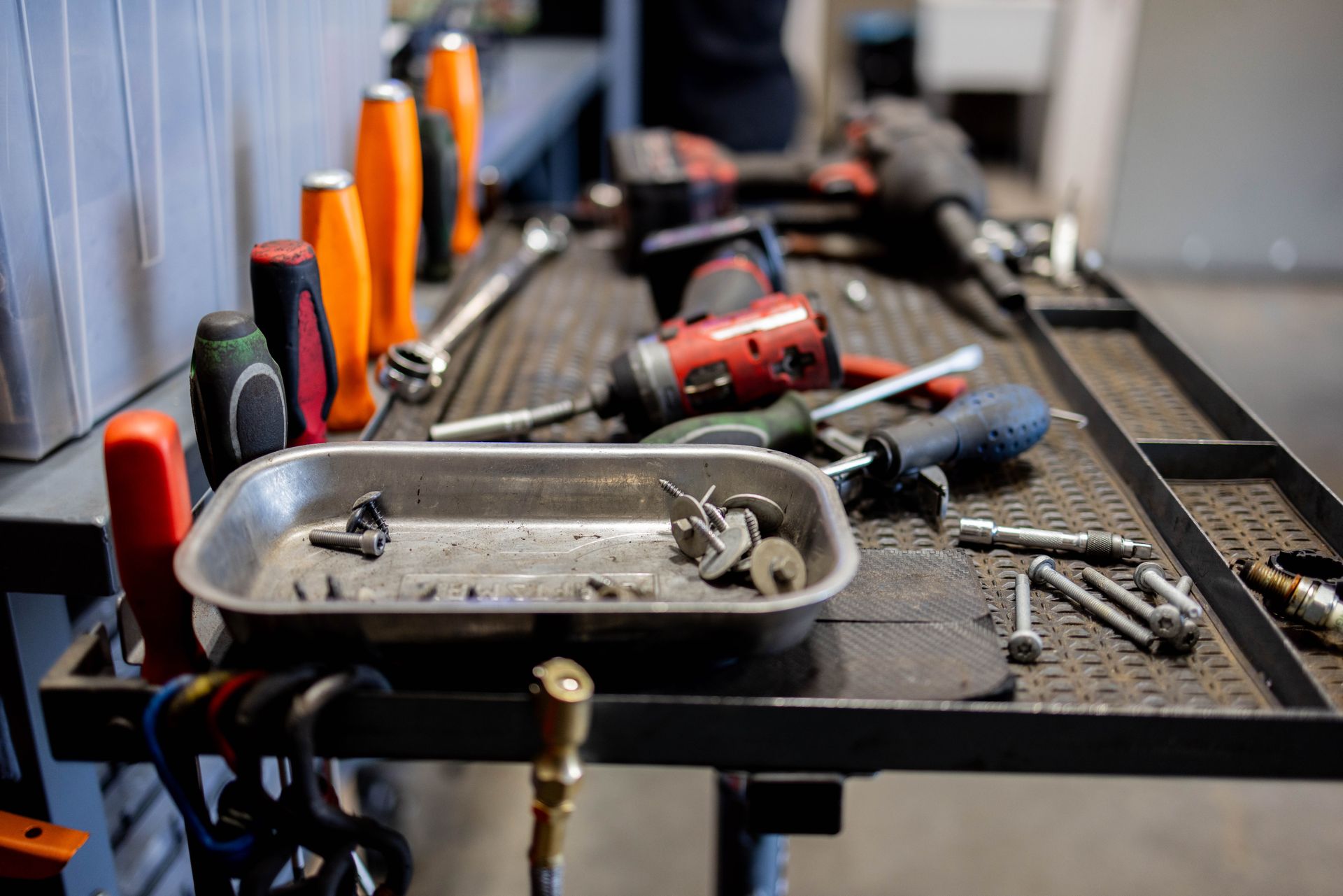 Tools on a workbench: wrenches, screwdrivers, an impact driver, and a tray of small parts in a garage. | Peak Euro