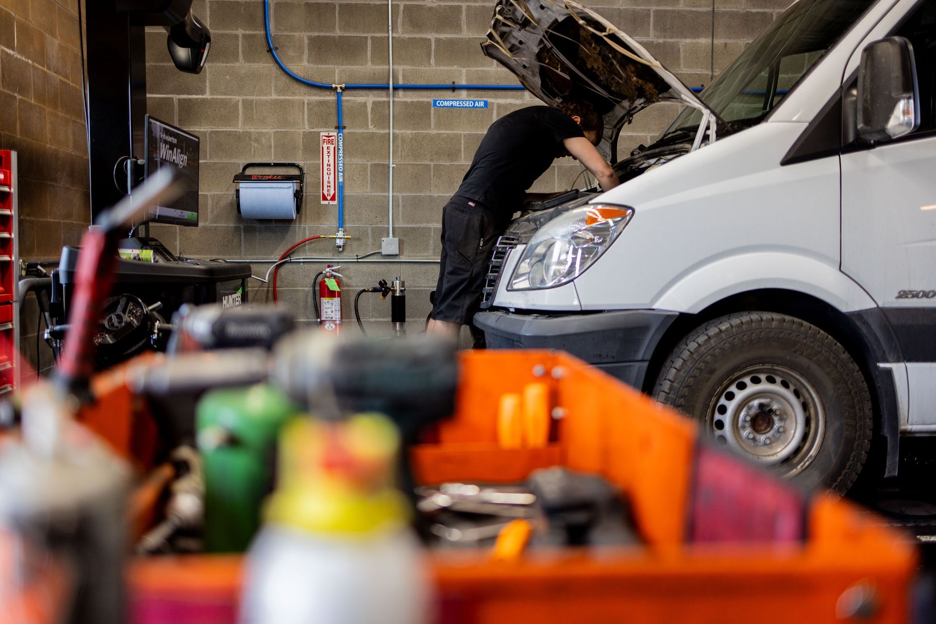 Mechanic working on a white van in a garage; orange toolbox in foreground. | Peak Euro