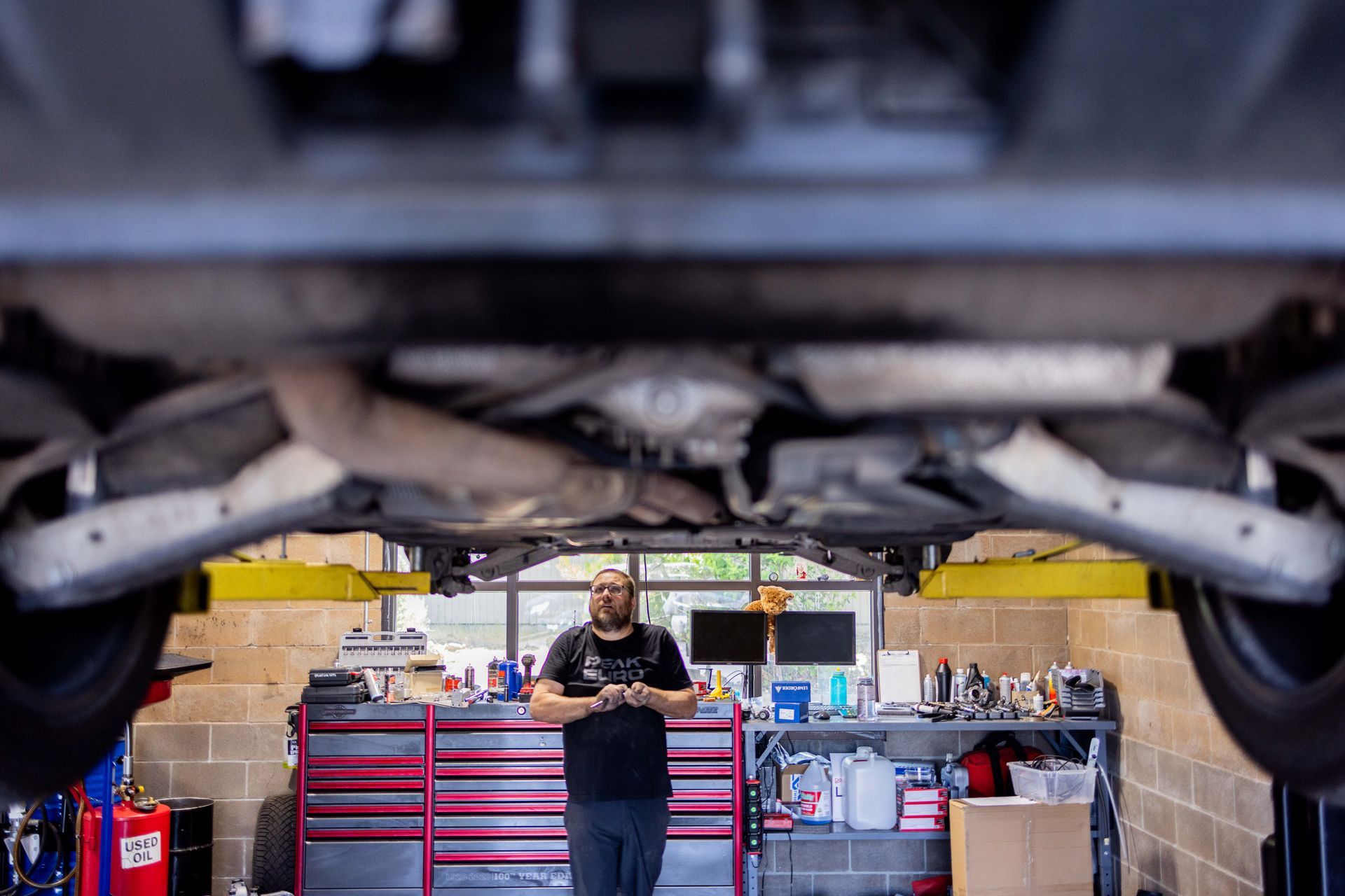 Mechanic under a car, tools in shop. | Peak Euro
