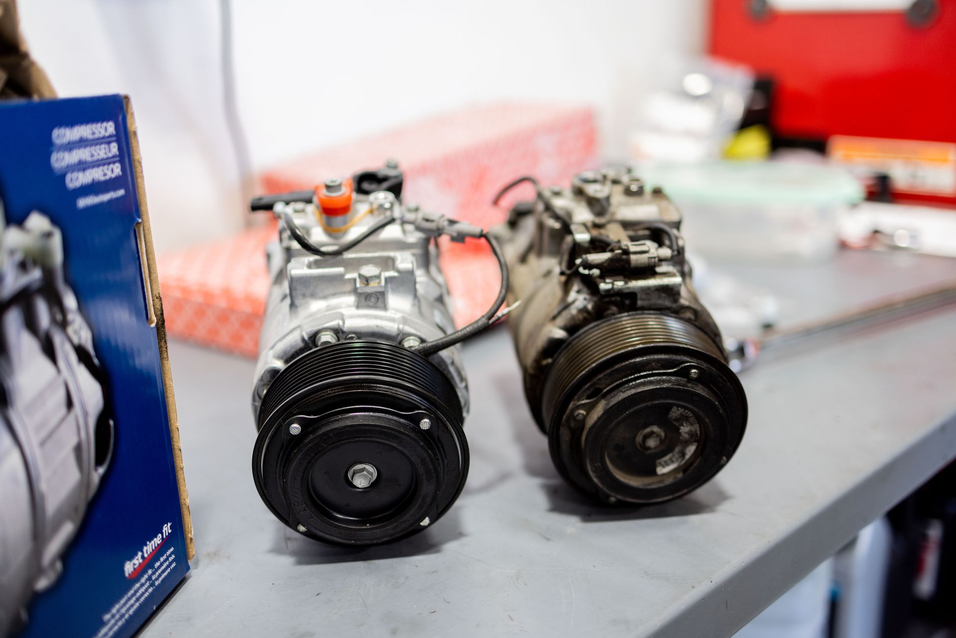 Two car air conditioning compressors, new and old, sit side-by-side on a table. | Peak Euro