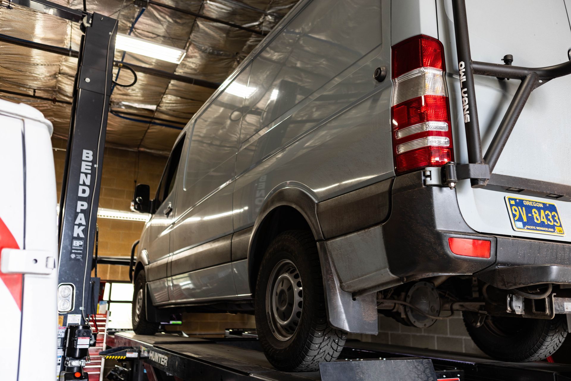 A silver van raised on a lift inside a garage, rear door open, with a BendPak lift. | Peak Euro