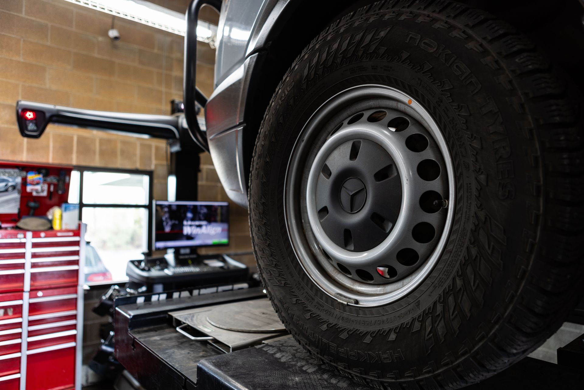 A van tire on a lift in a repair shop, being aligned. Grey and red tools are in the background. | Peak Euro