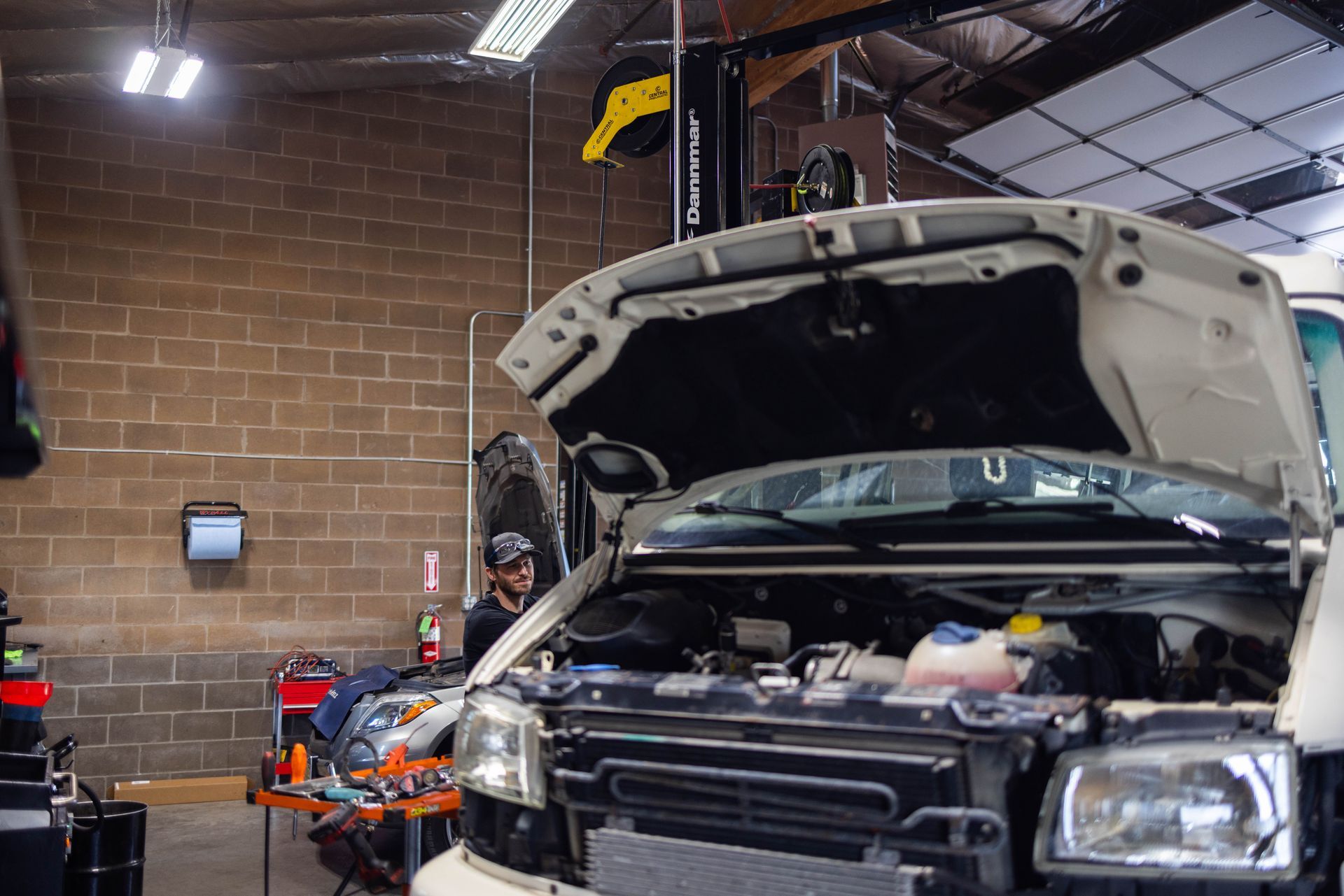 Mechanic working on a white van with the hood open in a garage. Tools and equipment visible. | Peak Euro
