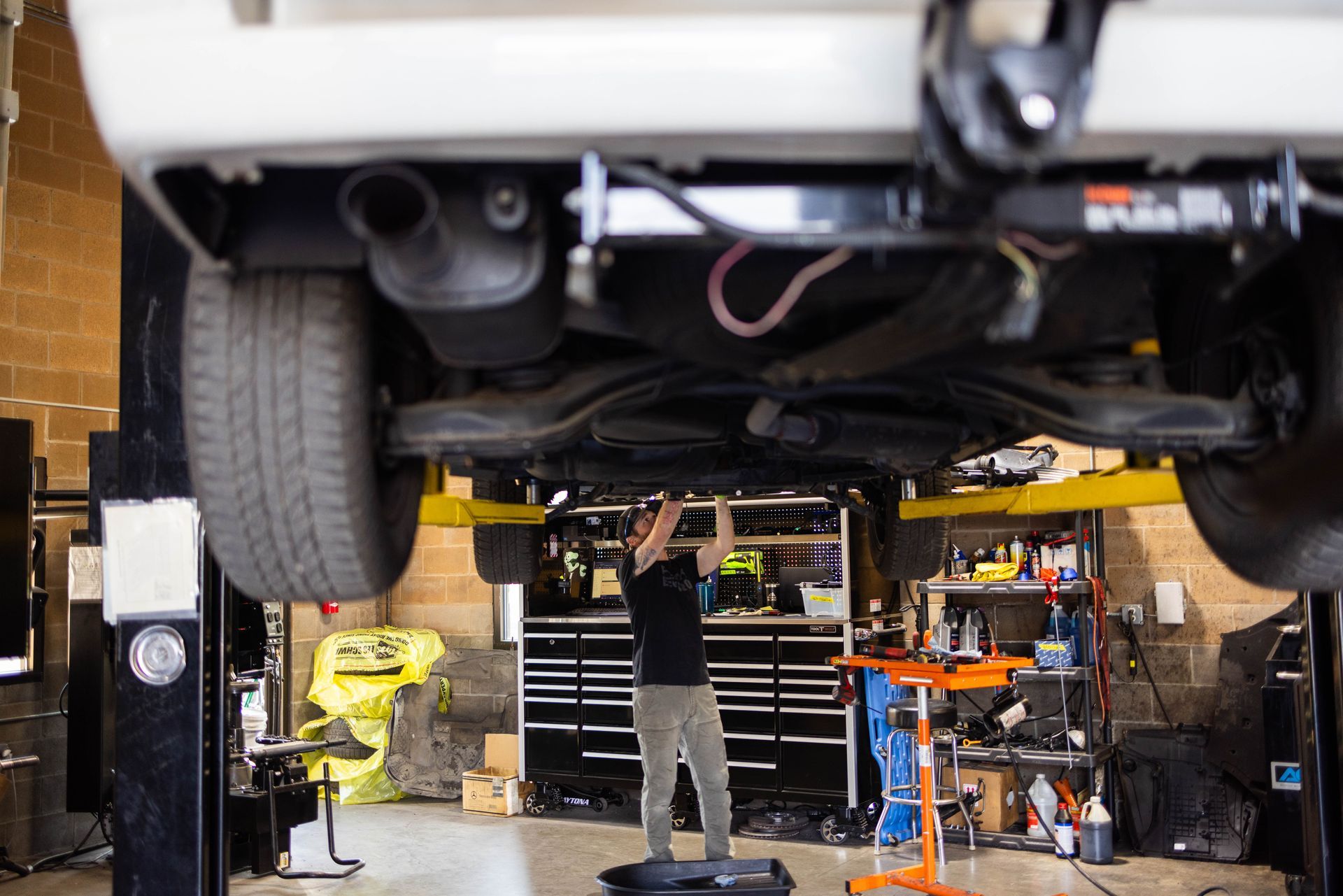 Mechanic working under a white car on a lift in a garage. | Peak Euro
