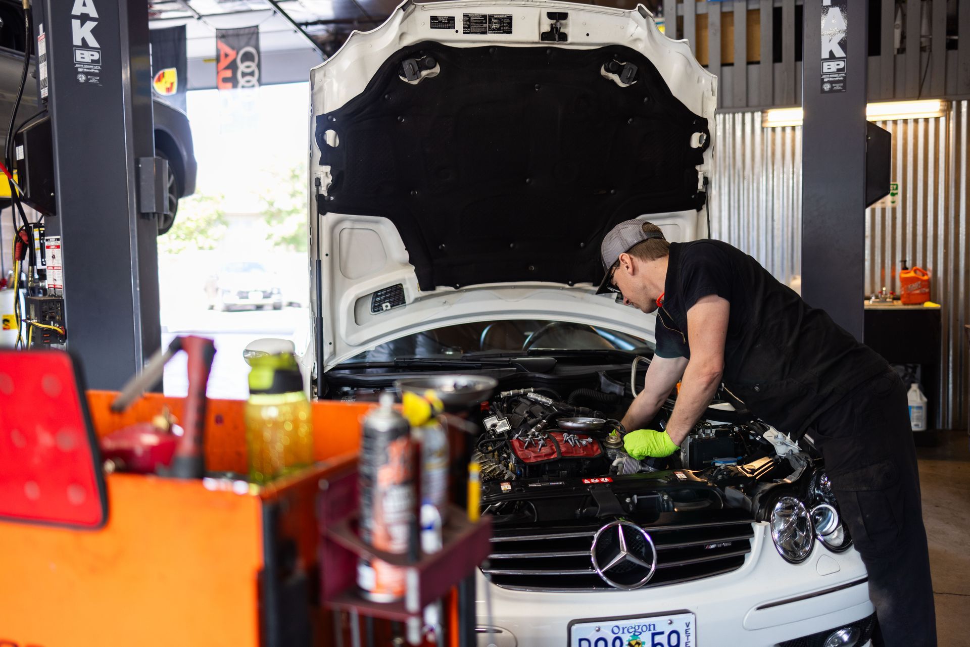 Mechanic working on a car engine in a garage; white car, tools, and a lift visible. | Peak Euro