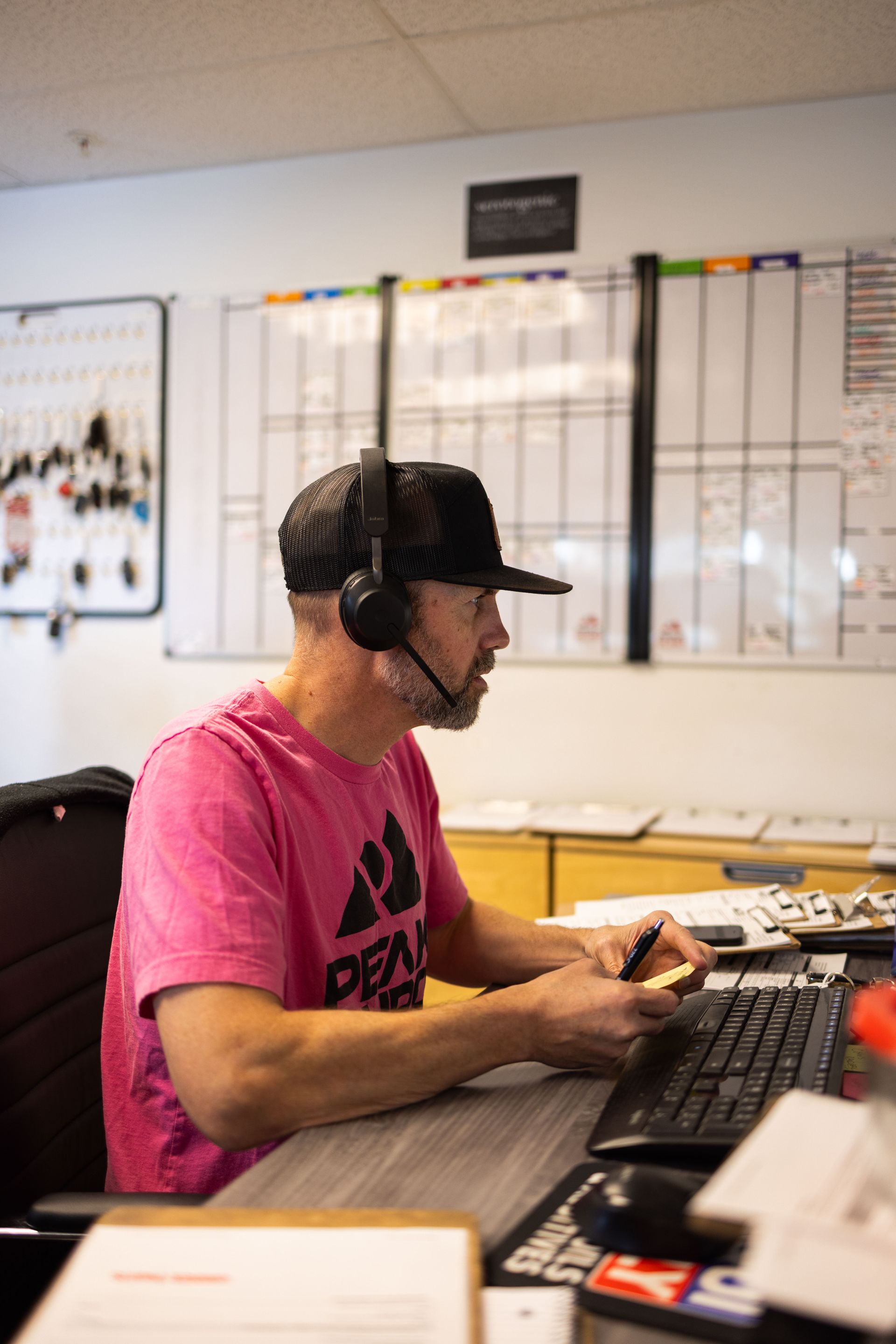Man in a pink shirt with headset, working at a computer in an office. | Peak Euro