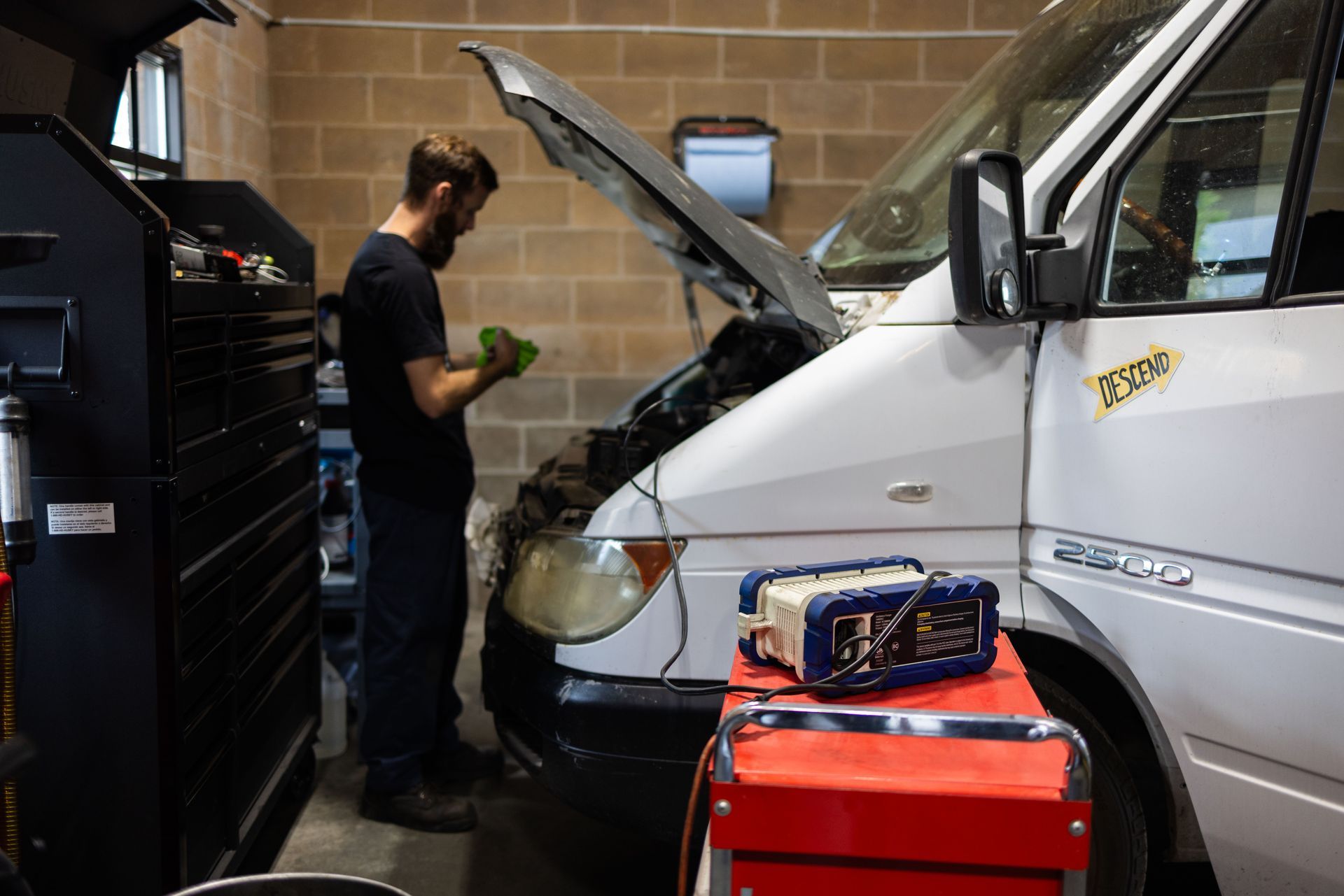Mechanic working on a white van with the hood open in a garage. A tool box and equipment are nearby. | Peak Euro